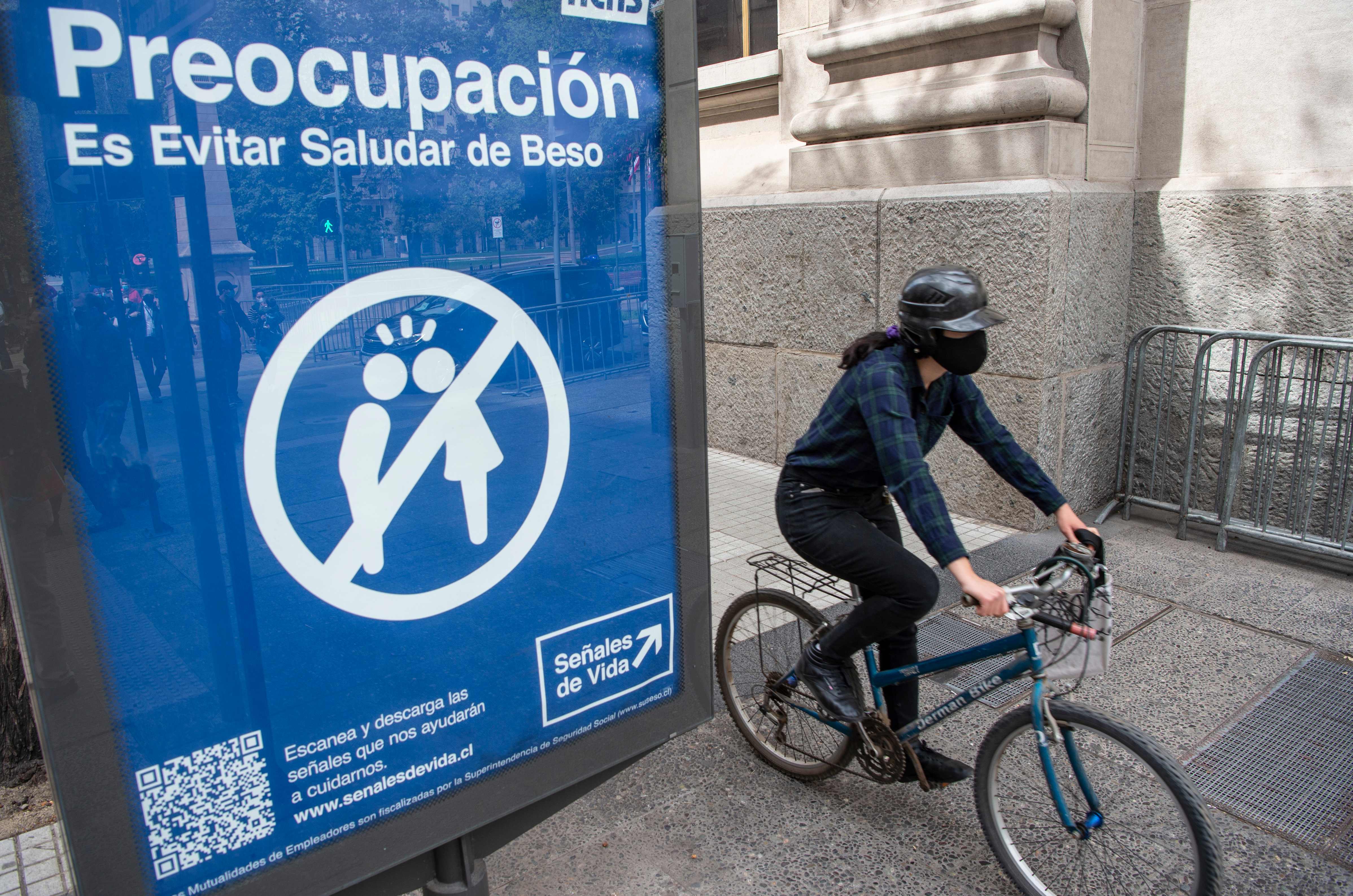Seorang pesepeda melintas di samping papan peringatan mengenai menjaga jarak sosial di Santiago, Cile.