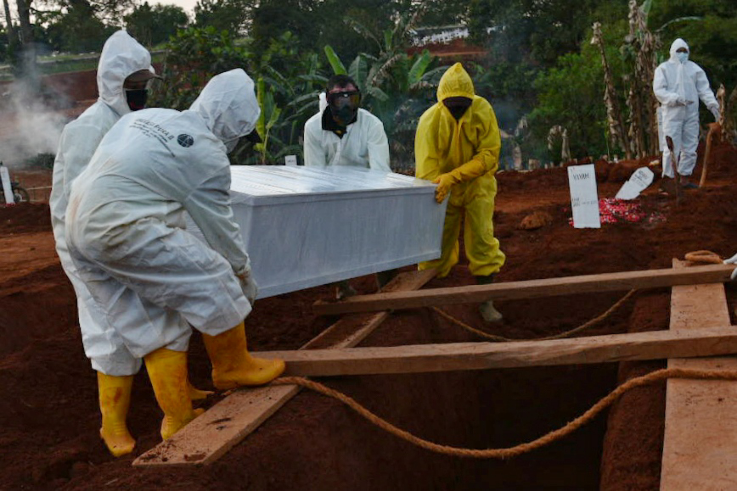 Petugas pemakaman penanganan jenazah pasien covid-19 menurunkan peti jenazah ke dalam pusara di TPU Pondok Ranggon, Jakarta Timur.