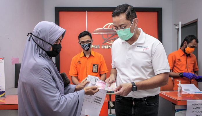 Menteri Sosial Juliari P Batubara (kanan) memberikan uang bantuan pemerintah kepada warga saat meninjau pencairan bantuan sosial tunai (BST)