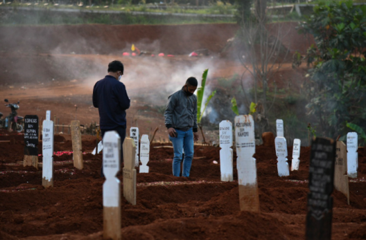 Petugas pemakaman penanganan jenazah pasien covid-19 menurunkan peti jenazah ke dalam pusara di TPU Pondok Ranggon, Jakarta Timur.