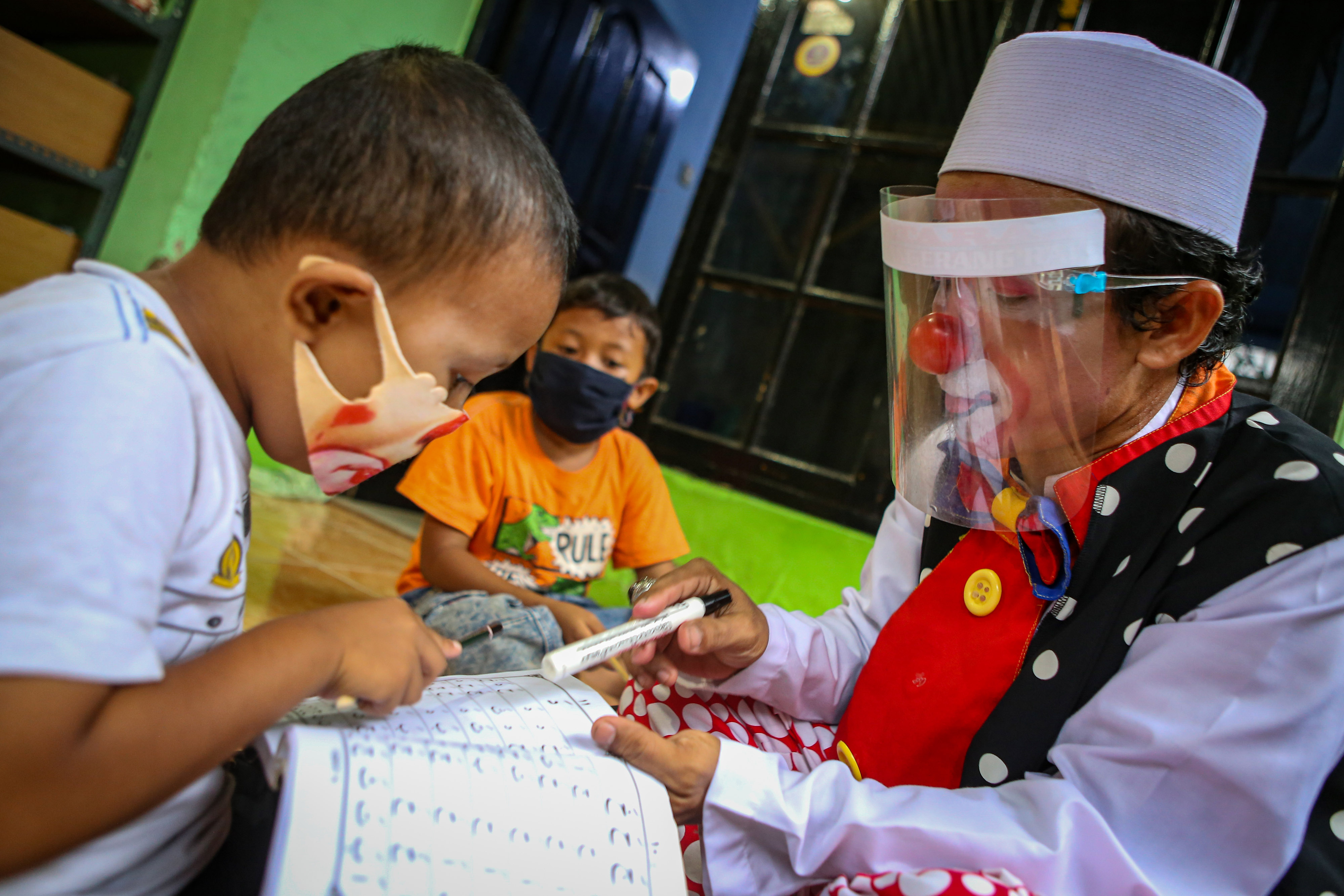 Seorang badut mengajar membaca Al Quran dengan tetap menerapkan protokol kesehatan.