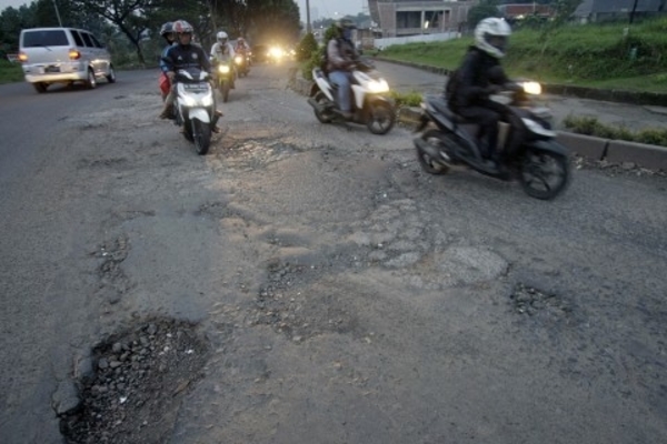Pengendara melintasi jalan rusak yang dipenuhi lubang di Jalan Boulevard, Grand Depok City, Depok, Jawa Barat. 