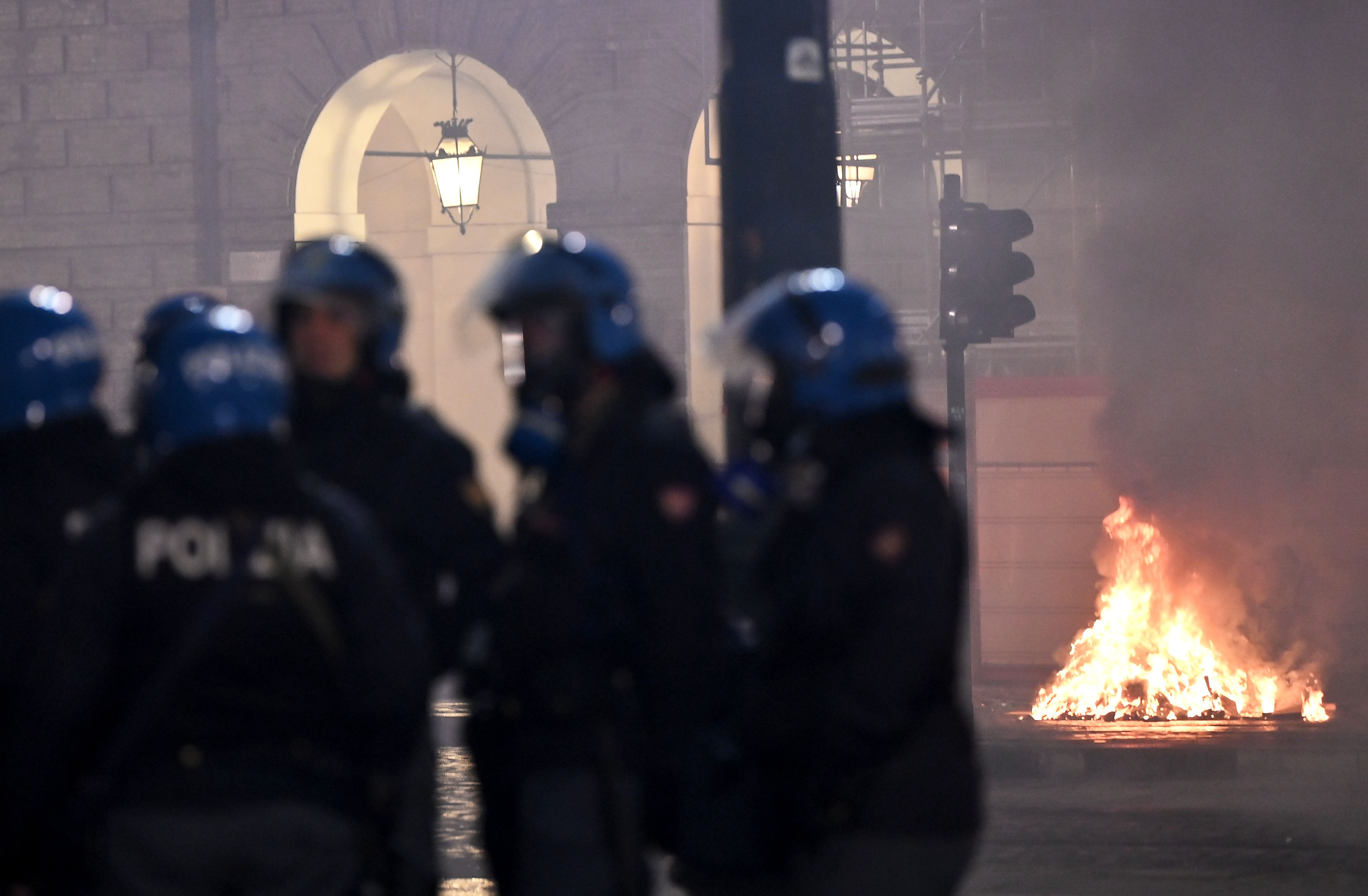 Polisi Italia berdiri di depan gerobak yang dibakar dalam aksi demonstrasi menetang pembatasan baru di Turin.