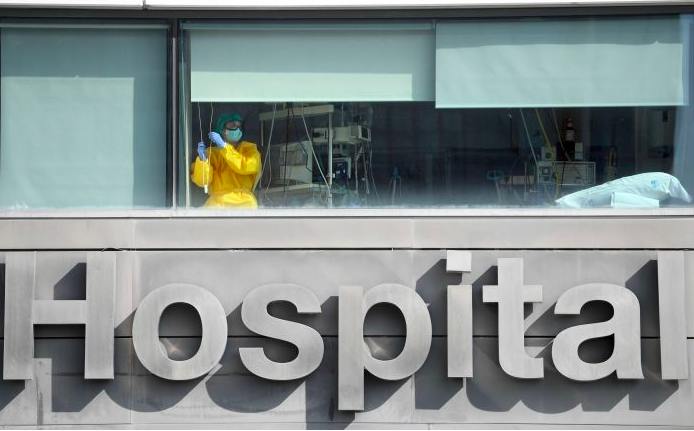 Petugas kesehatan memakai APD membuka tirai di ruang perawatan covid-19 RS La Paz, Madrid, Spanyol.  