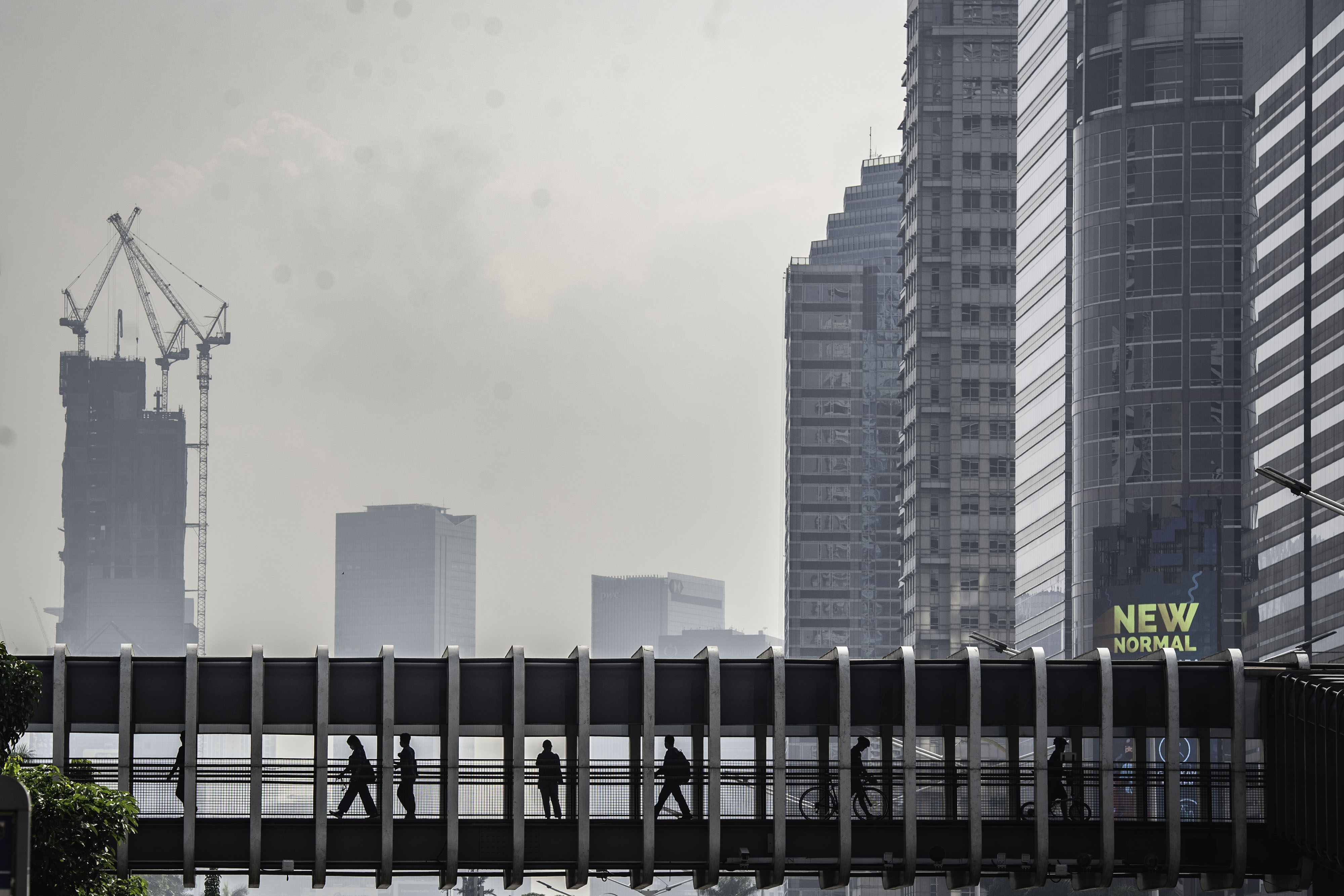  Warga berjalan di jembatan penyeberangan orang dengan latar belakang gedung perkantoran di Jakarta, Sabtu (26/9/2020).