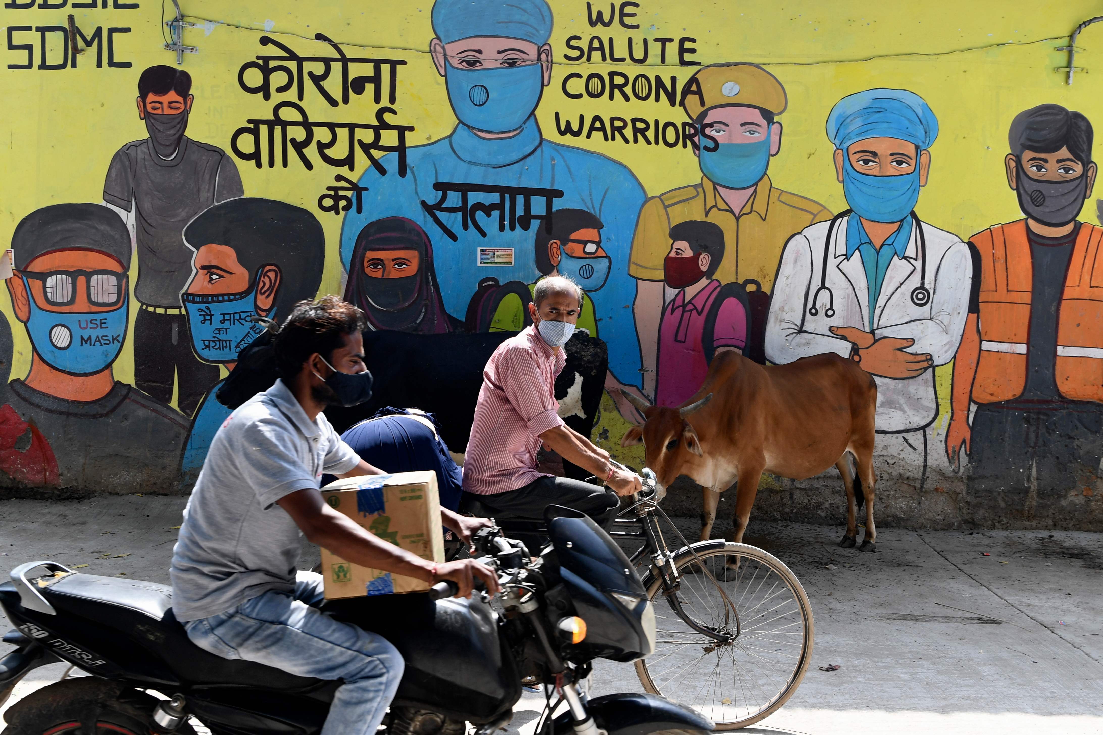 Pengendara melintasi mural terkait covid-19 di New Delhi, India.