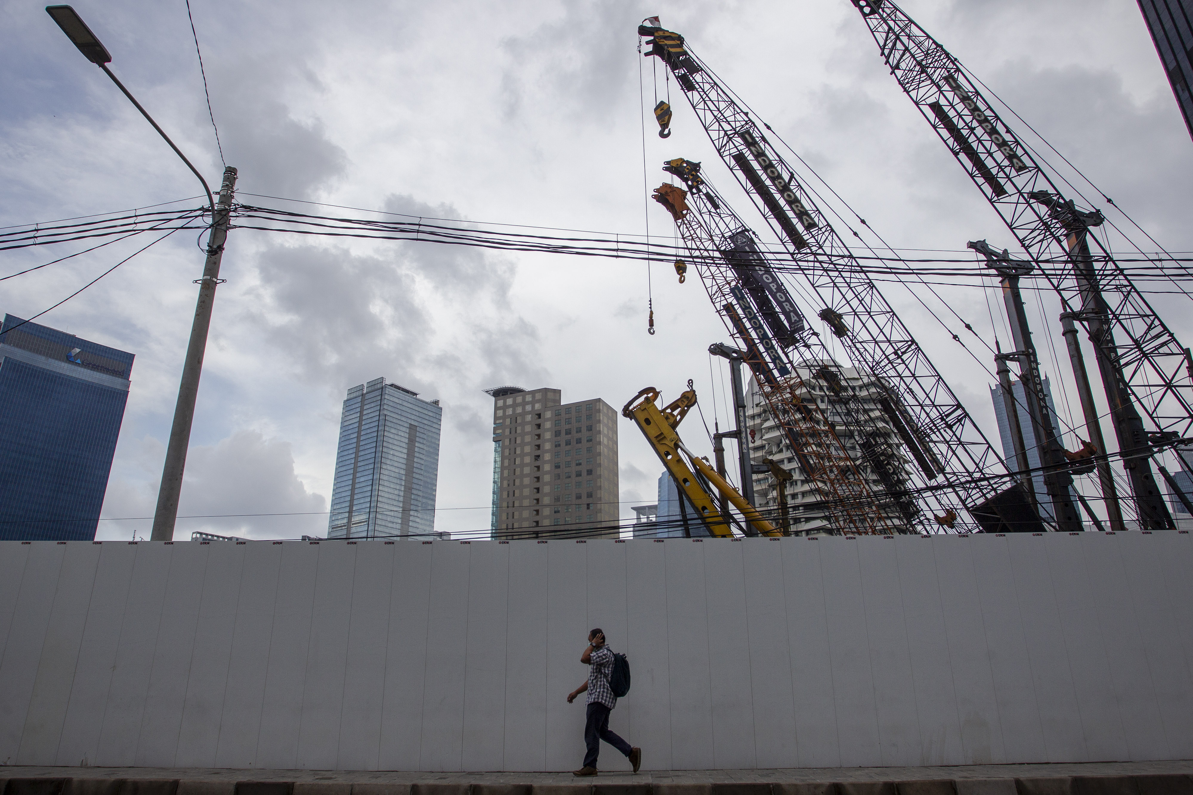 Warga berjalan dengan latar belakang proyek pembangunan gedung bertingkat di kawasan Bendungan Hilir, Jakarta, Selasa (20/10/2020).