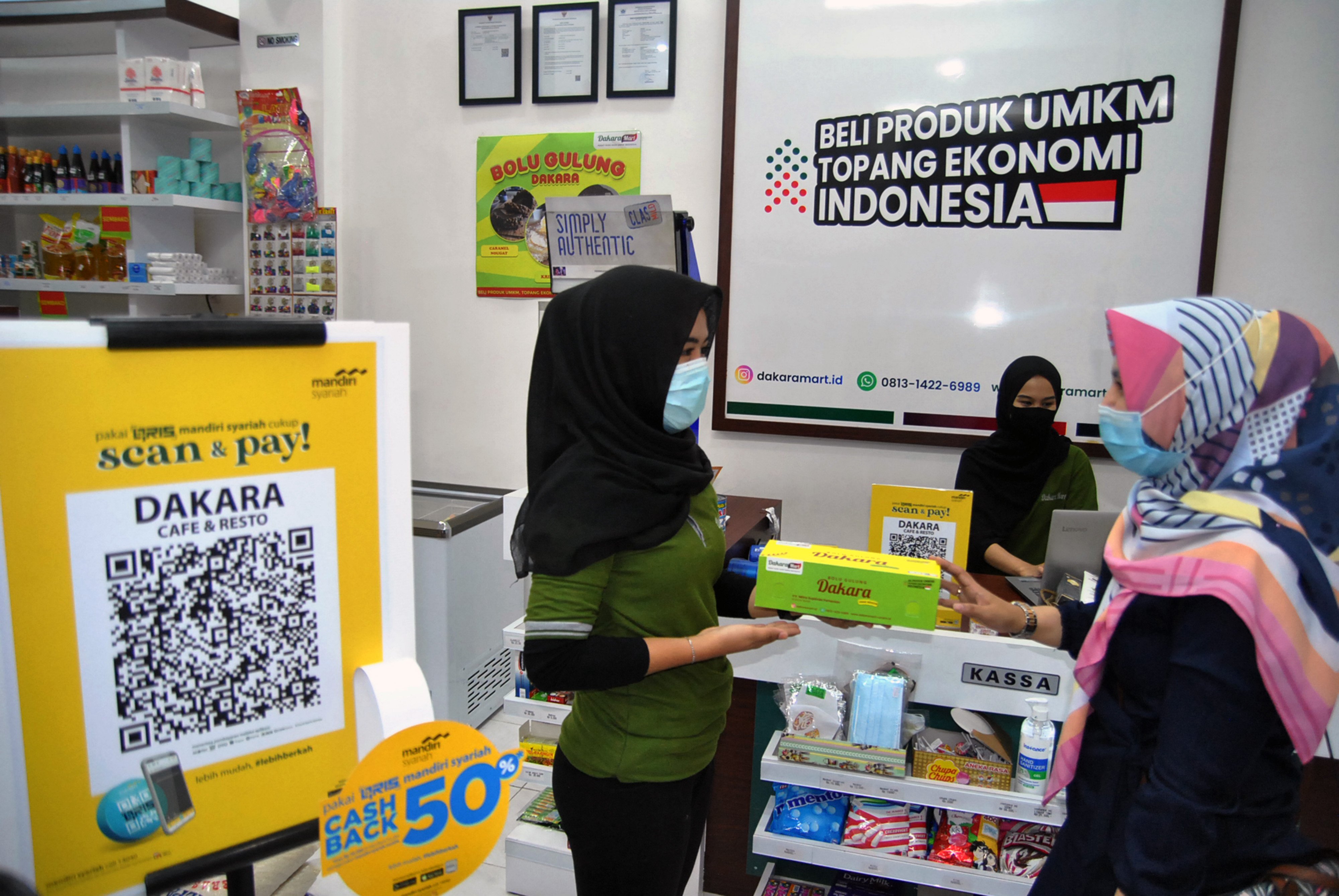 Nasabah Bank Mandiri Syariah berbincang dengan pelayan toko saat menggunakan layanan digital di Pusat Oleh-oleh UMKM Indonesia Dakara Mart.