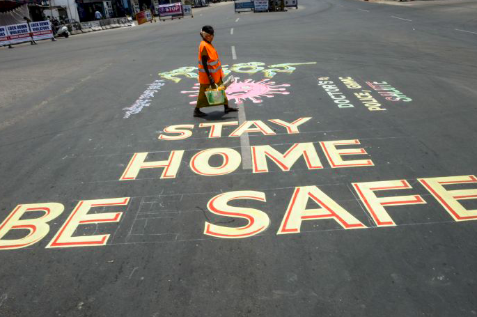 Seorang pekerja di India melintasi jalan yang dihiasi grafiti terkait pesan melawan covid-19.