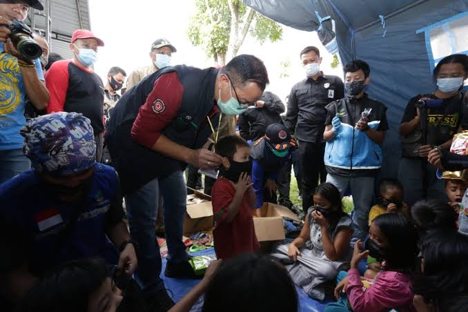 Menteri Sosial Juliari P Batubara  (tengah) membantu seorang anak memakai masker.
