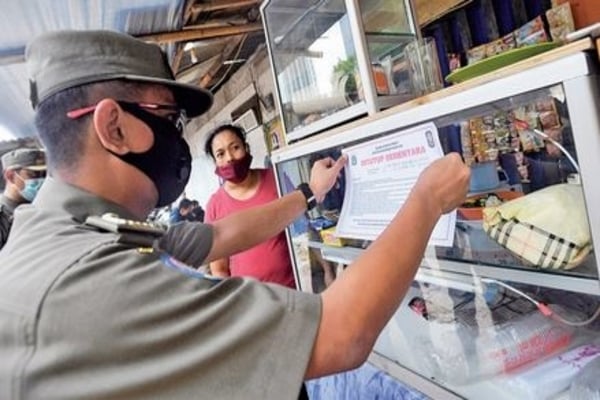Anggota Satpol PP memasang pengumuman sanksi penutupan sementara warung yang kedapatan masih melayani makan di tempat, Setiabudi, Jakarta