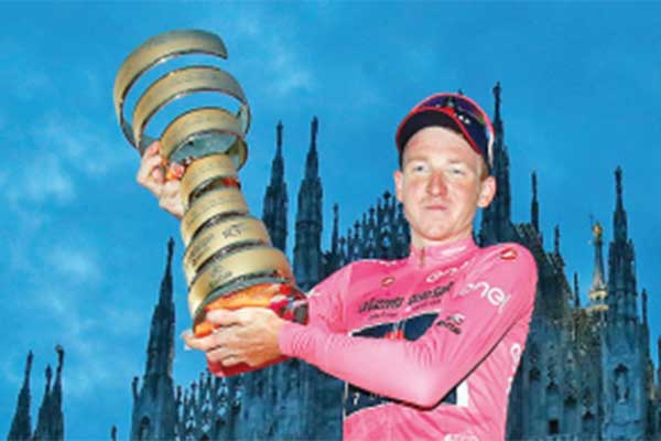 Pemenang Giro d’Italia 2020 Tao Geoghegan Hart mengenakan jersey jingga sembari mengangkat trofi 