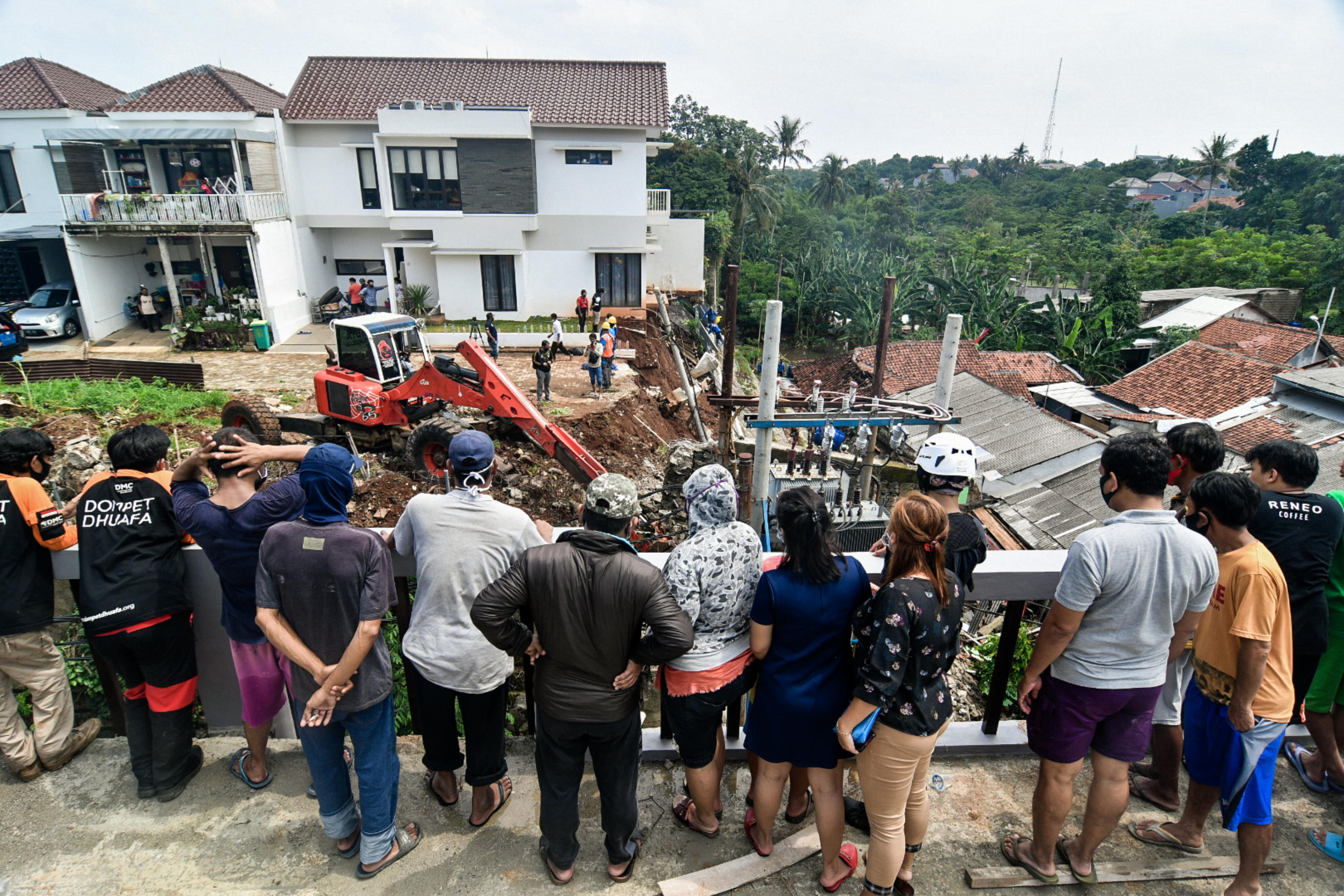 Warga melihat petugas menggunakan alat berat saat sedang mengamankan dinding yang hampir longsor di kawasan Ciganjur, Jagakarsa, Jakarta.