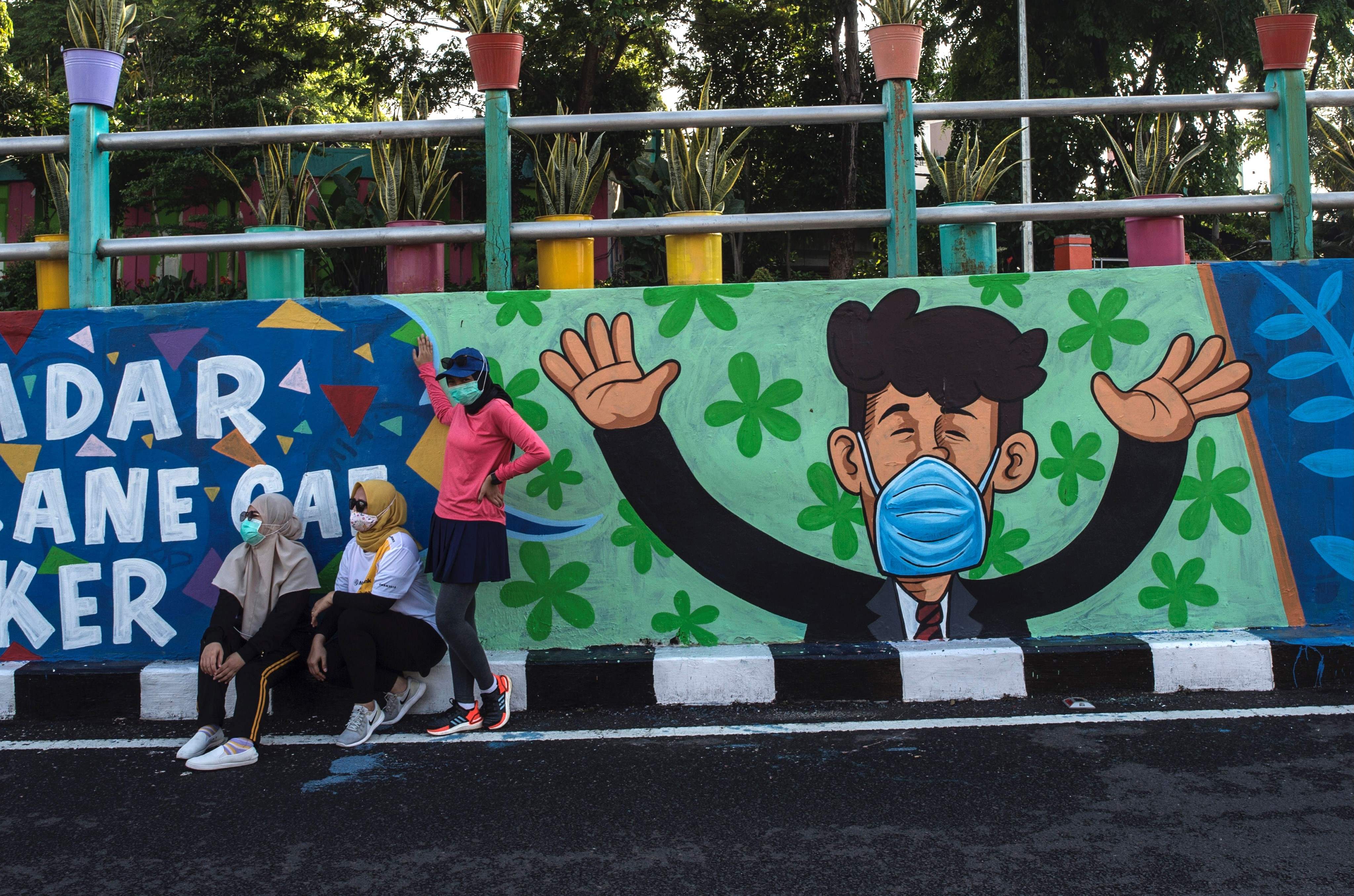 Warga berpose di depan poster yang mengimbau warga untuk mengenakan masker di Surabaya, Jawa Timur.