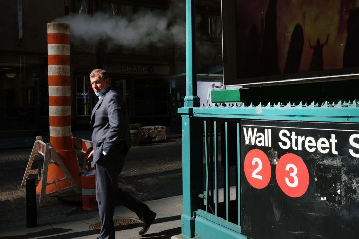 Seorang pria memakai masker berjalan di sekitar area Wall Street New York. Saham-saham Wall Street dibuka menguat hari ini, Selasa (20/10)