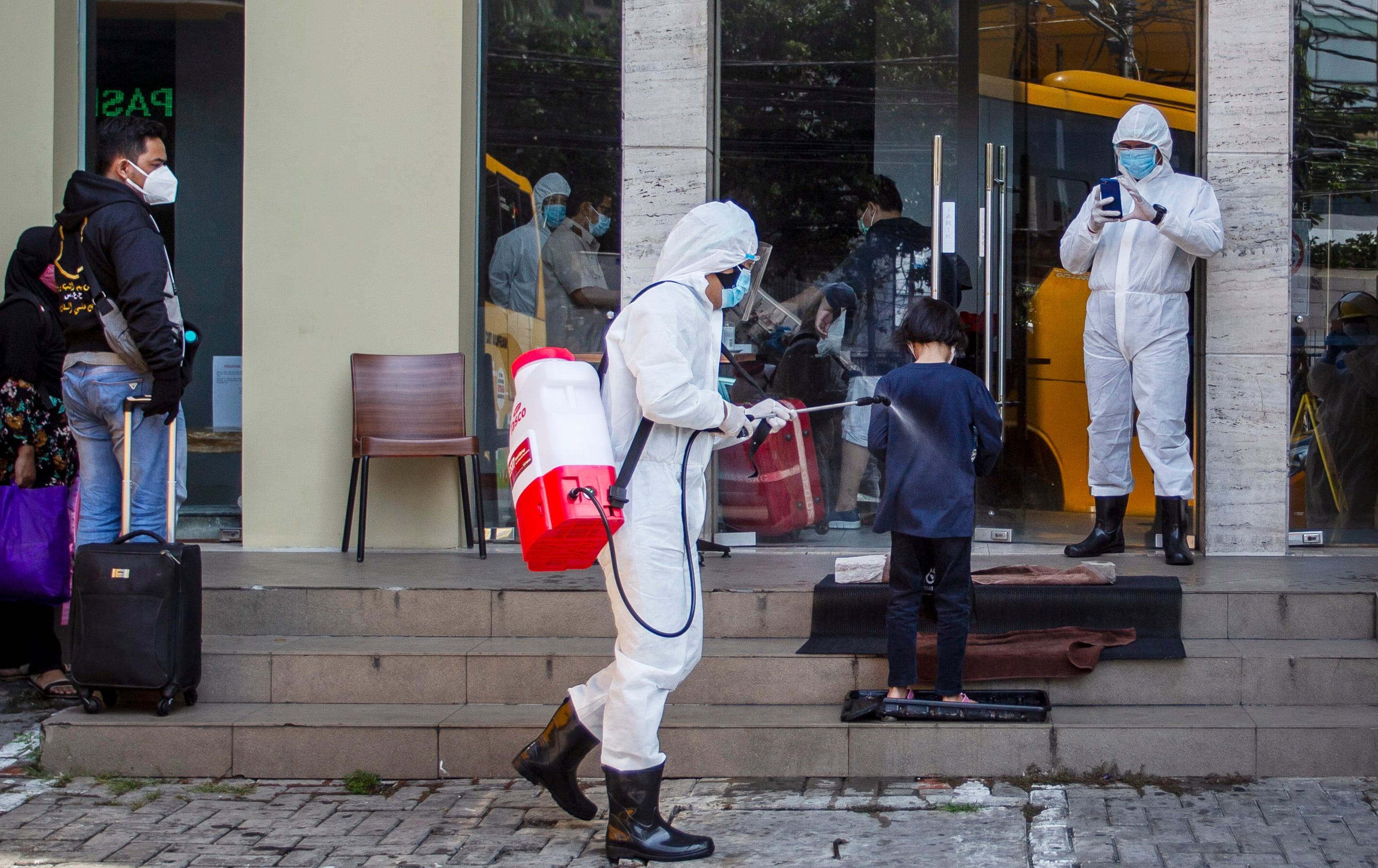 Petugas medis meyemprotkan cairan disinfektan kepada pasien covid-19 berstatus OTG sebelum memasuki hotel di Jakarta, Senin (28/9).