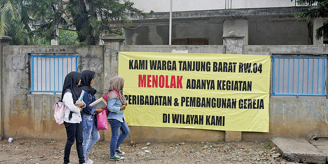 Warga melintas di dekat spanduk penolakan adanya kegiatan peribadatan sekaligus pembangunan gereja di Jalan Tanjung Barat Lama No 148 A.