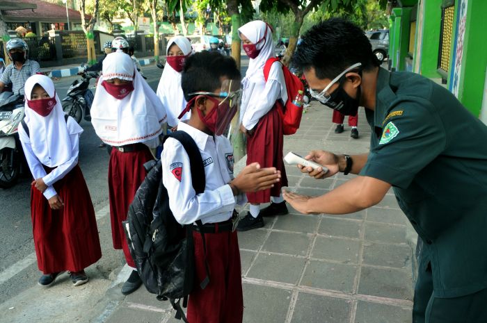 Guru memeriksa suhu tubuh siswa saat hari pertama Pembelajaran Tatap Muka (PTM) di SDN Lawangan Daya 2, Pamekasan, Jawa Timur.  