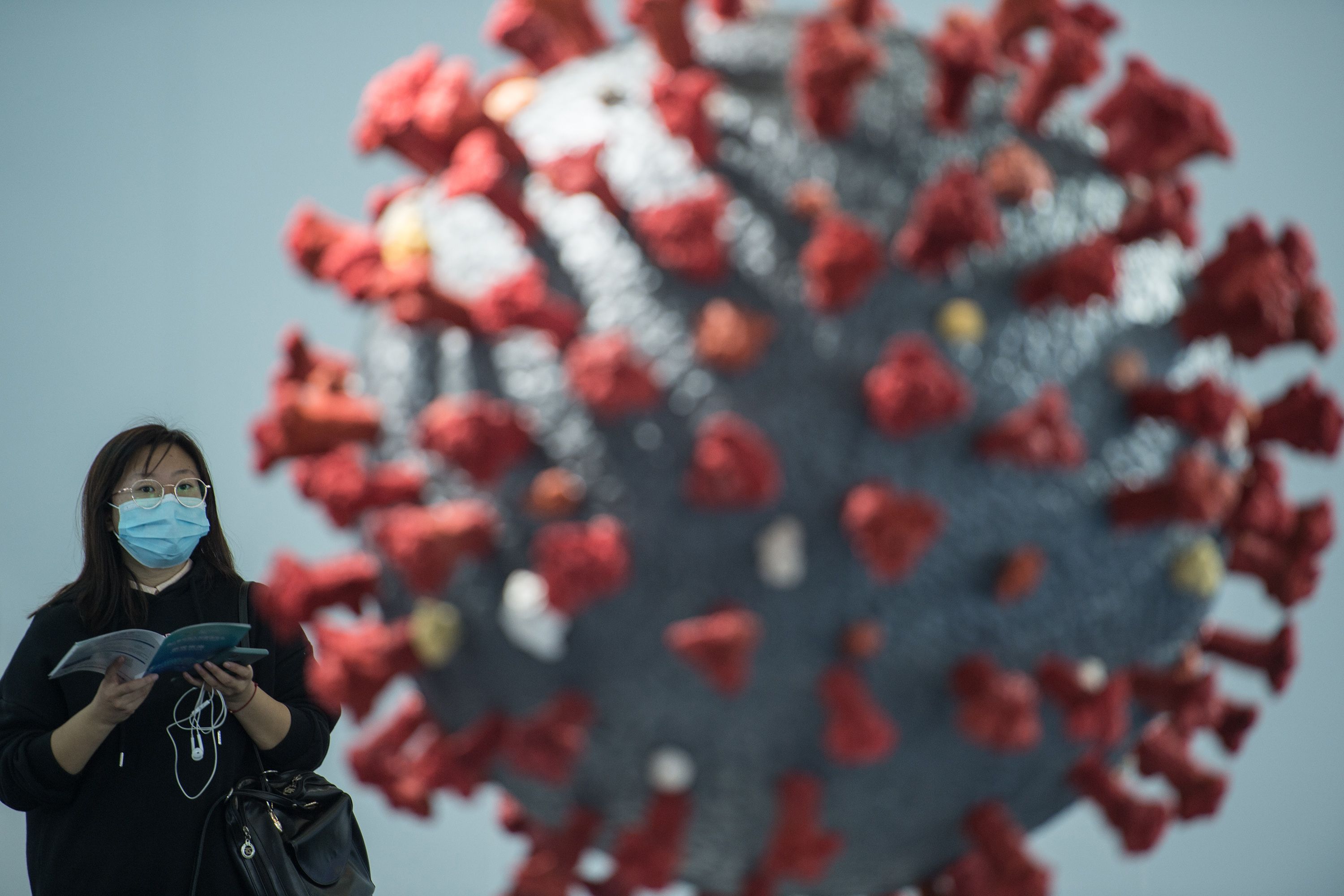 Seorang pengunjung mengenakan masker melihat model virus korona di World Health Expo di Tuhan, Tiongkok.