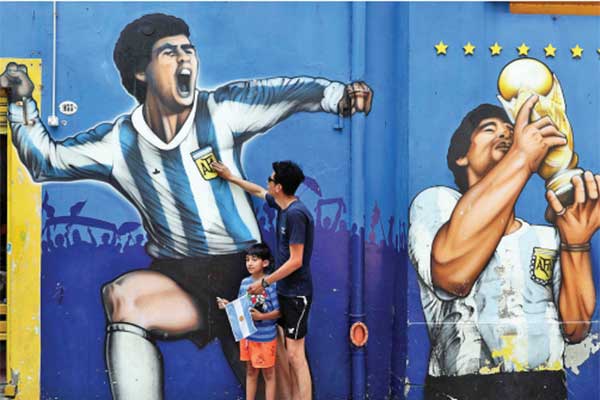 Seorang ayah bersama putranya berdiri menyentuh mural bergambar legenda sepak bola Argentina Diego Armando Maradona