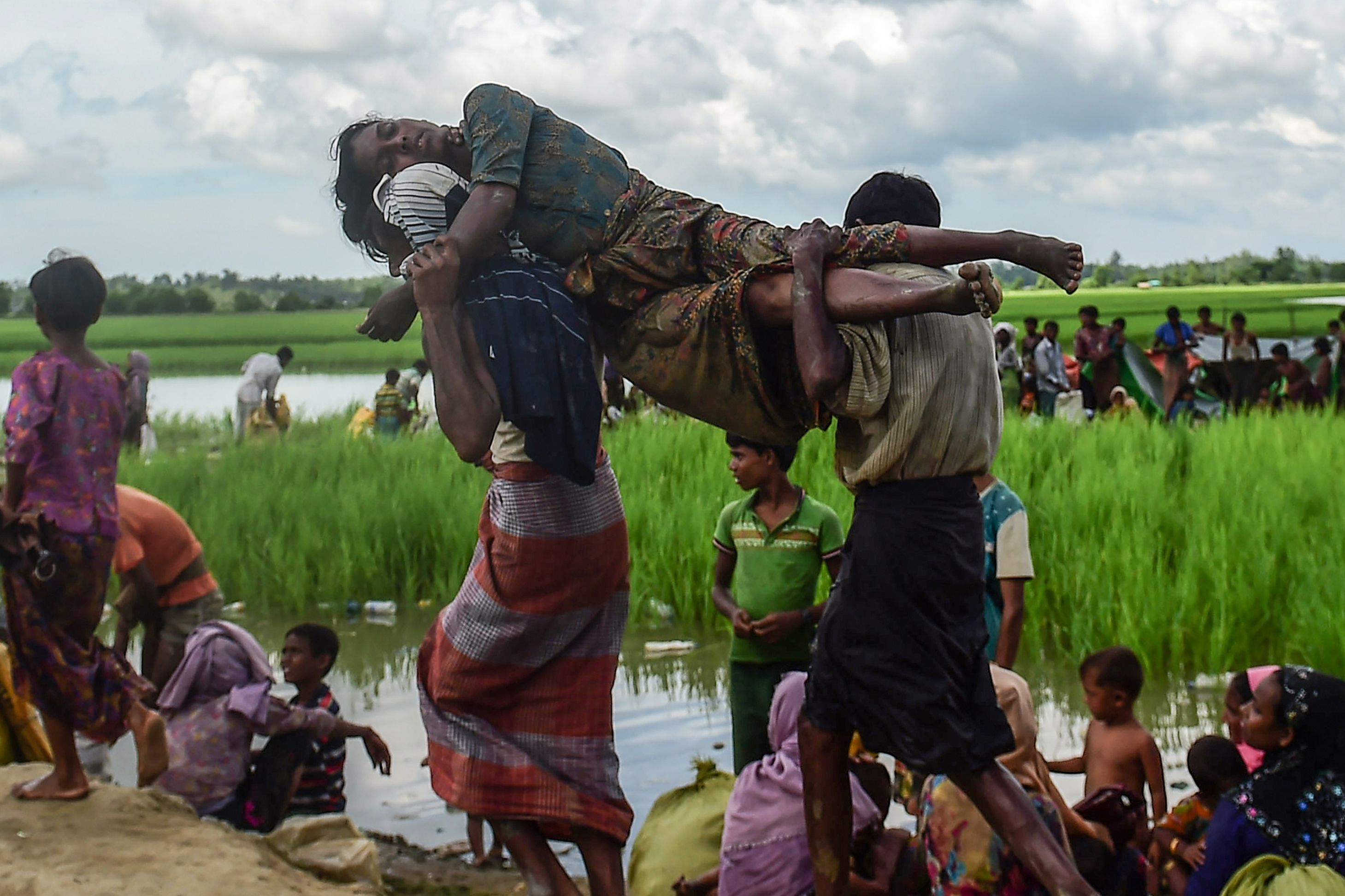 Seorang perempuan Rohingya digendong dua kerabatnya saat menyeberangi perbatasan Myanmar-Bangladesh.