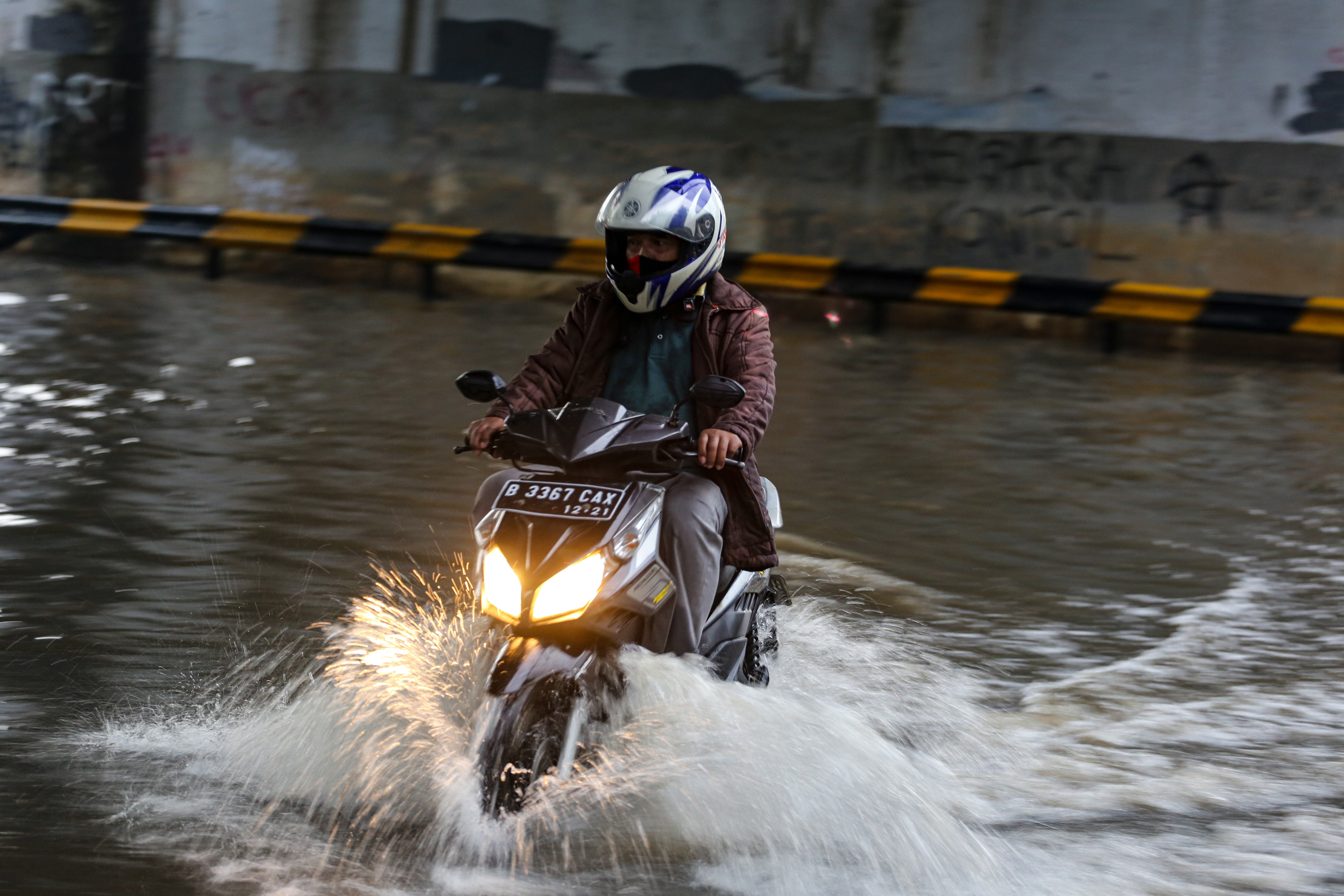 Pengendara motor melintas di genangan air di Jati Uwung, Kota Tangerang, Banten.