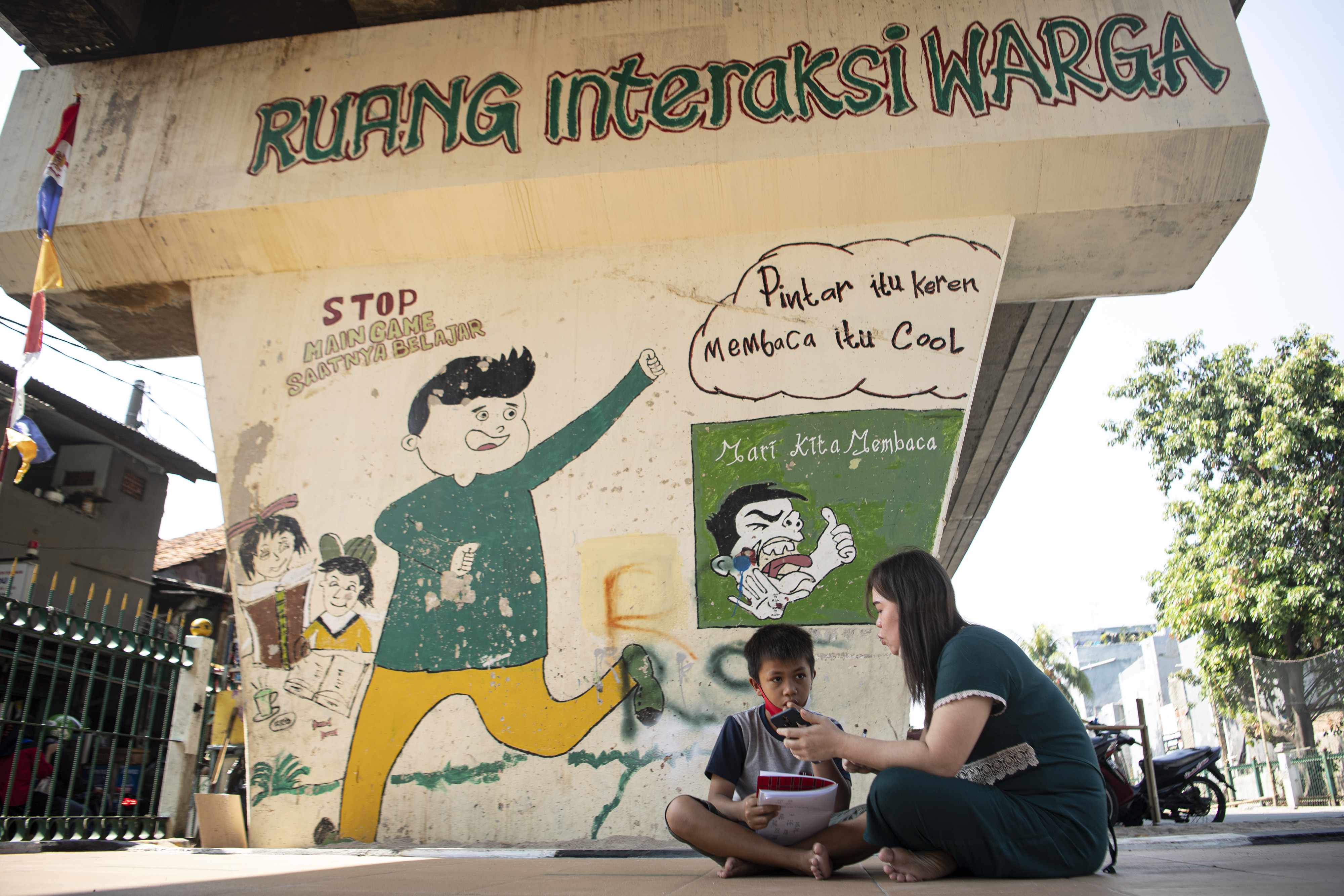 Orang tua siswa membimbing anaknya belajar daring memanfaatkan internet gratis di kolong rel kereta api Mangga Besar, Jakarta, Rabu(26/8).