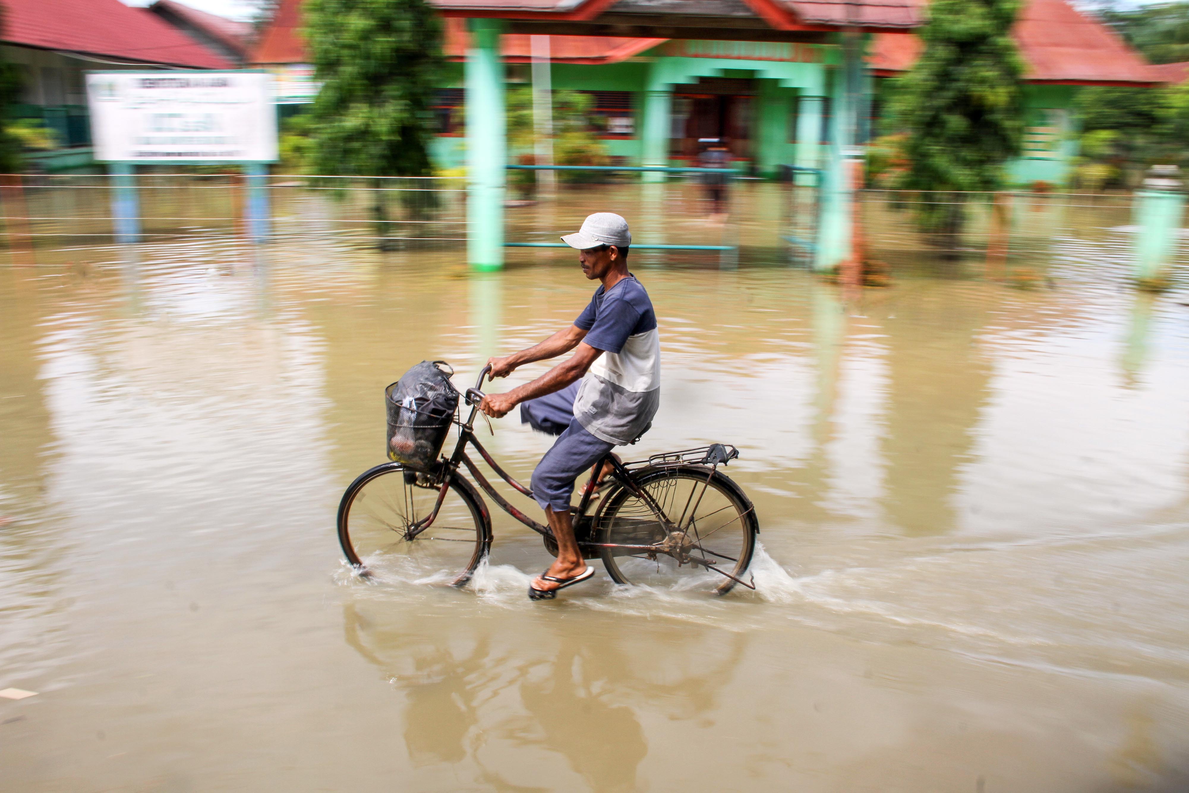 Warga melintas dengan sepeda ditengah banjir meredam sekolah MTsN Matang Kuli, Aceh Utara, Rabu (17/6).