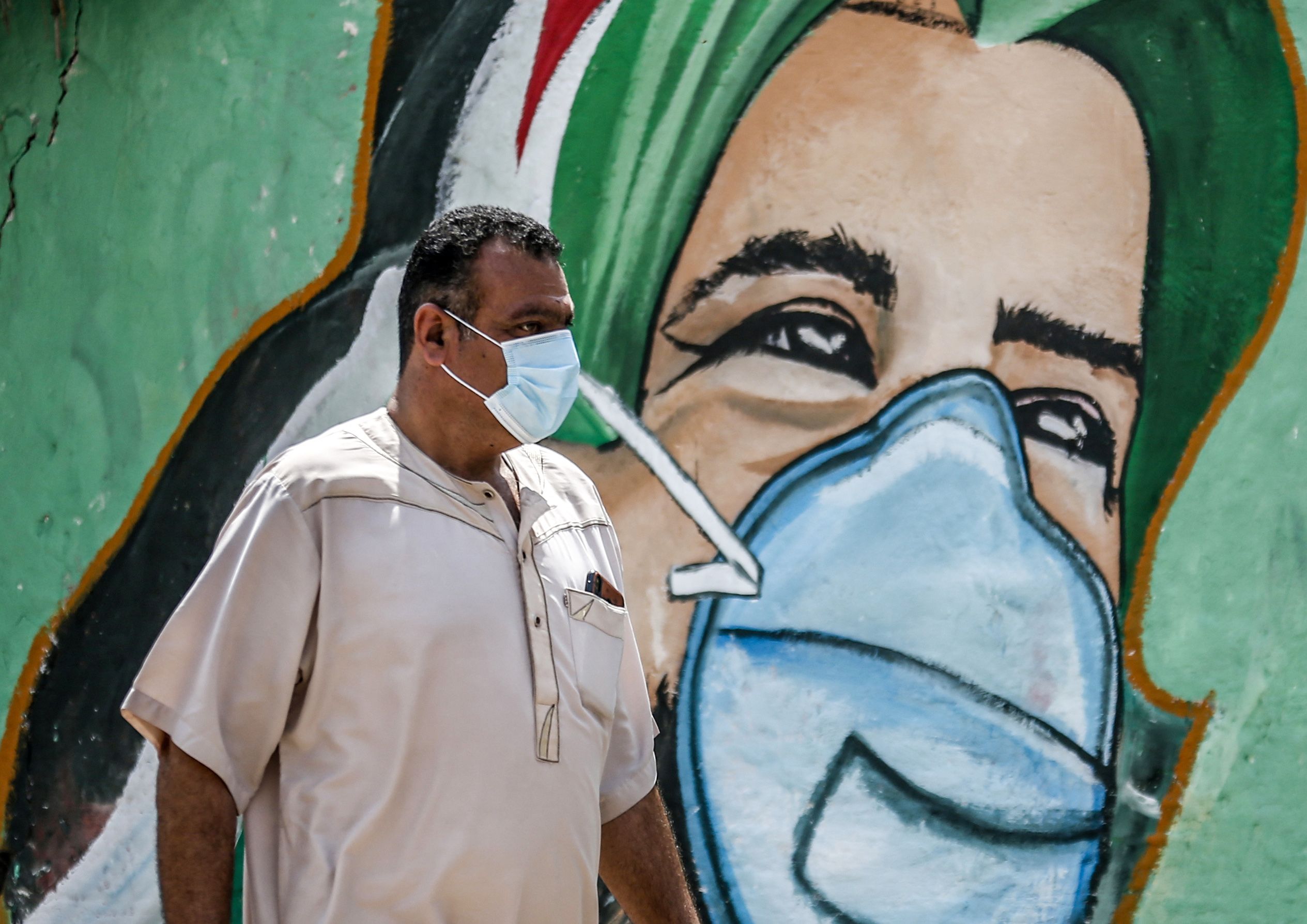 Seorang pria melintasi mural terkait kampanye covid-19 di wilayah Jalur Gaza.