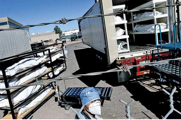 Petugas memasukkan ratusan jenazah covid-19 yang dibungkus plastik ke dalam trailer yang didinginkan di area parkir di El Paso, AS.