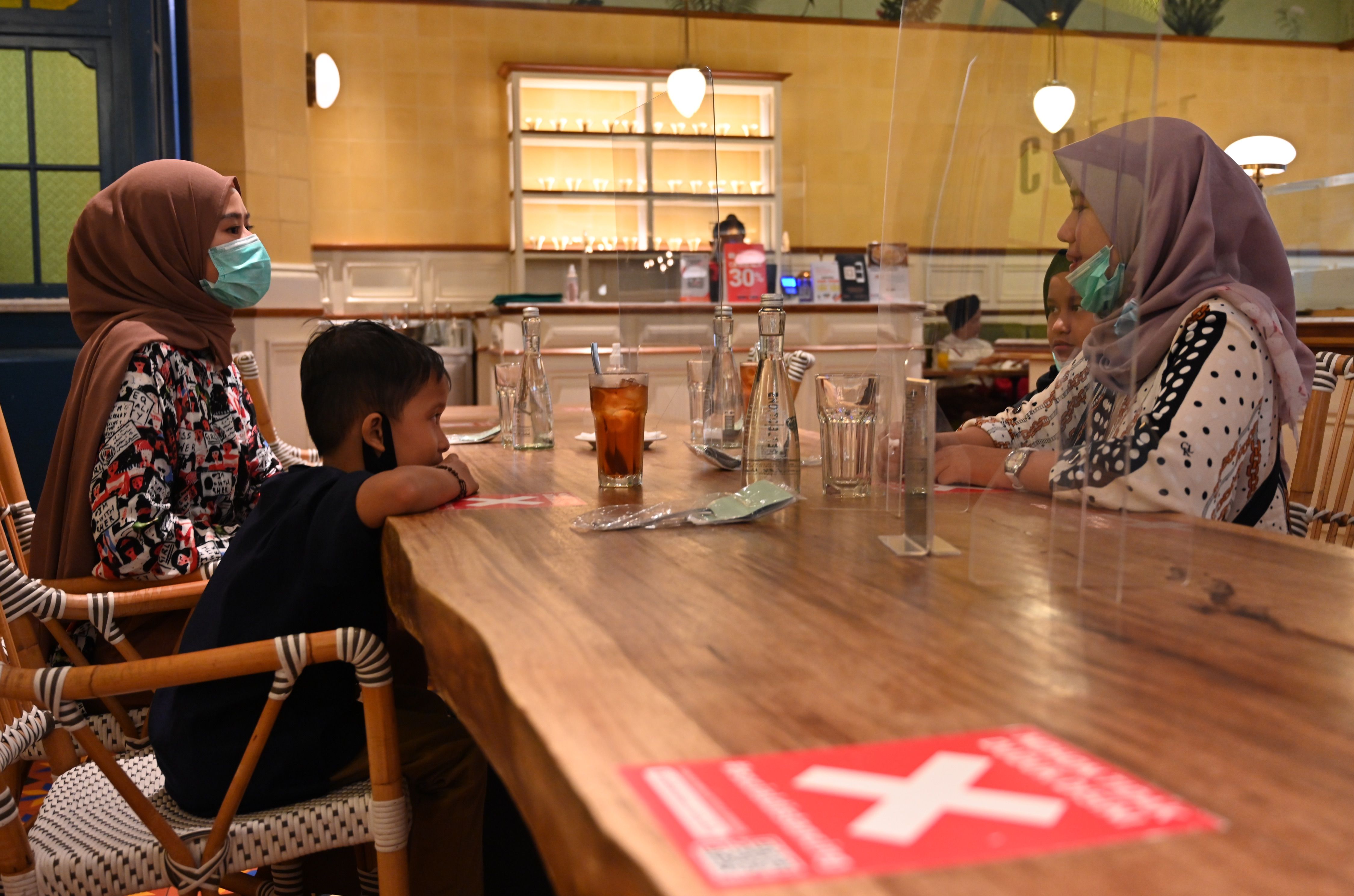 Warga mengenakan masker duduk di meja dengan partisi plastik di sebuah restoran di Jakarta.