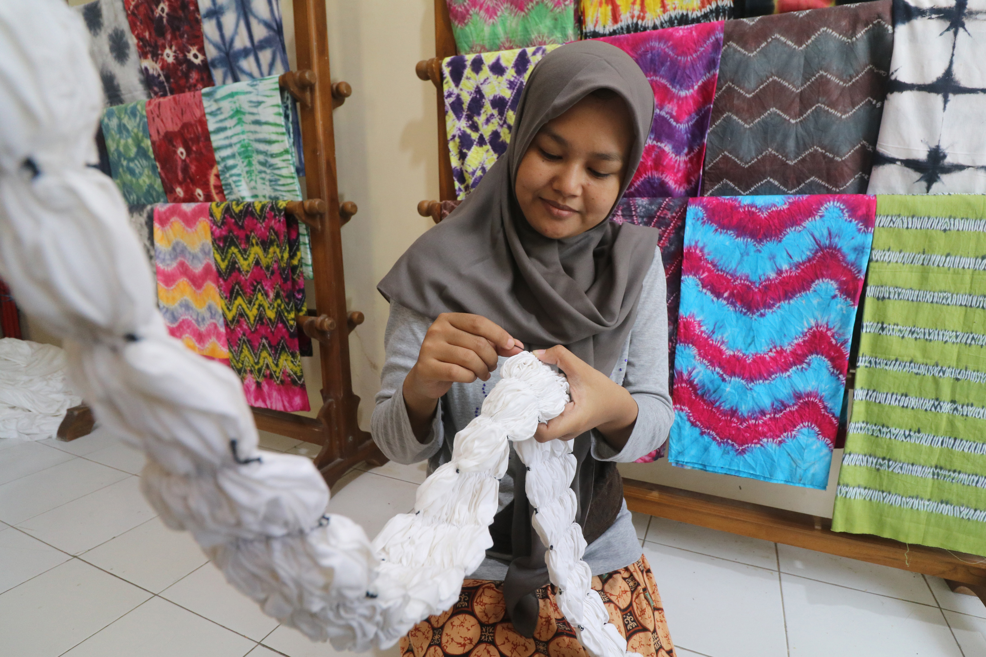  Perajin mengikat kaos putih polos sebagai proses pewarnaan teknik ikat celup atau bisa disebut dengan tie dye di Kota Kediri, Jawa Timur.