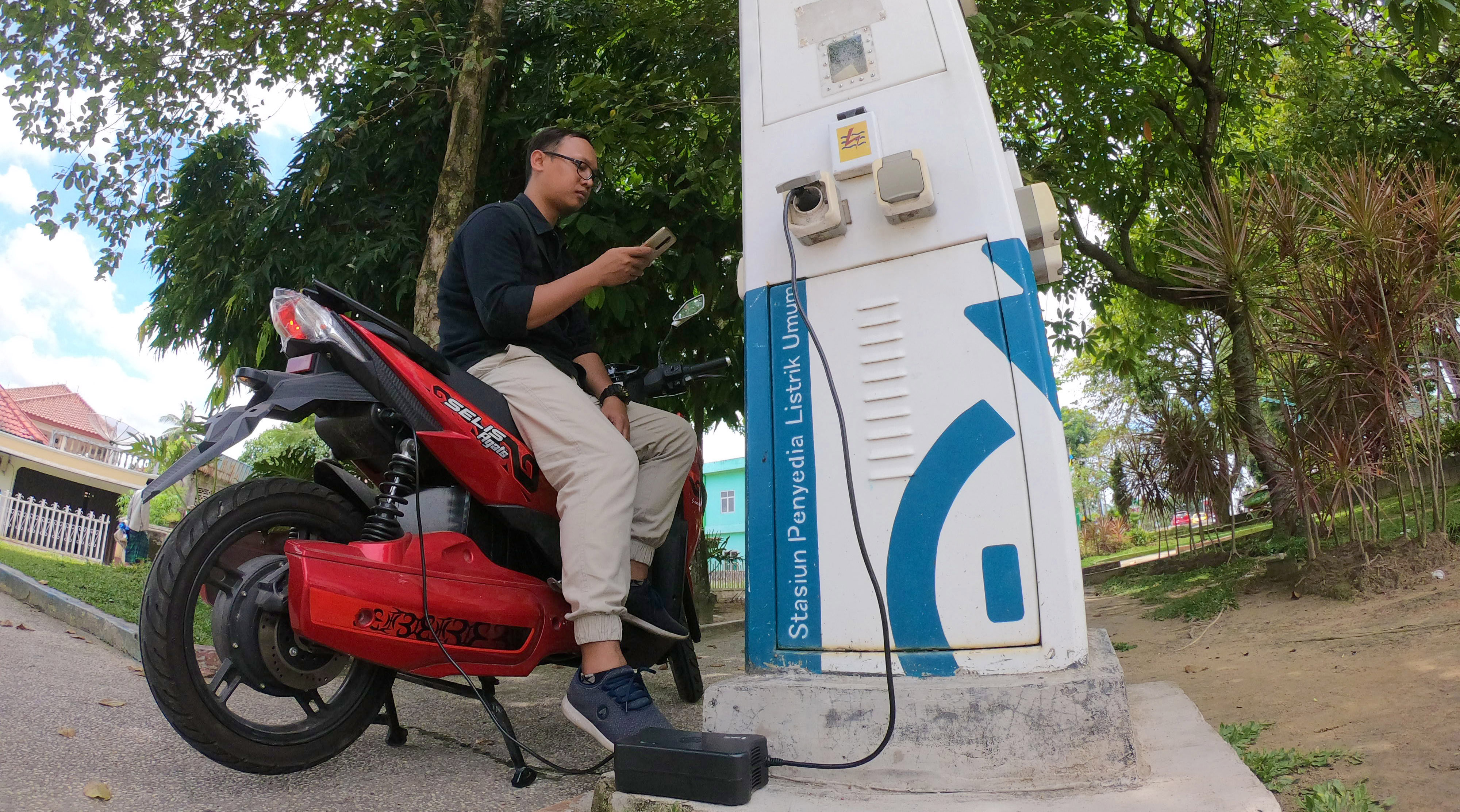 Pengendara sepeda motor listrik mengisi daya di Stasiun Penyedia Listrik Umum (SPLU)