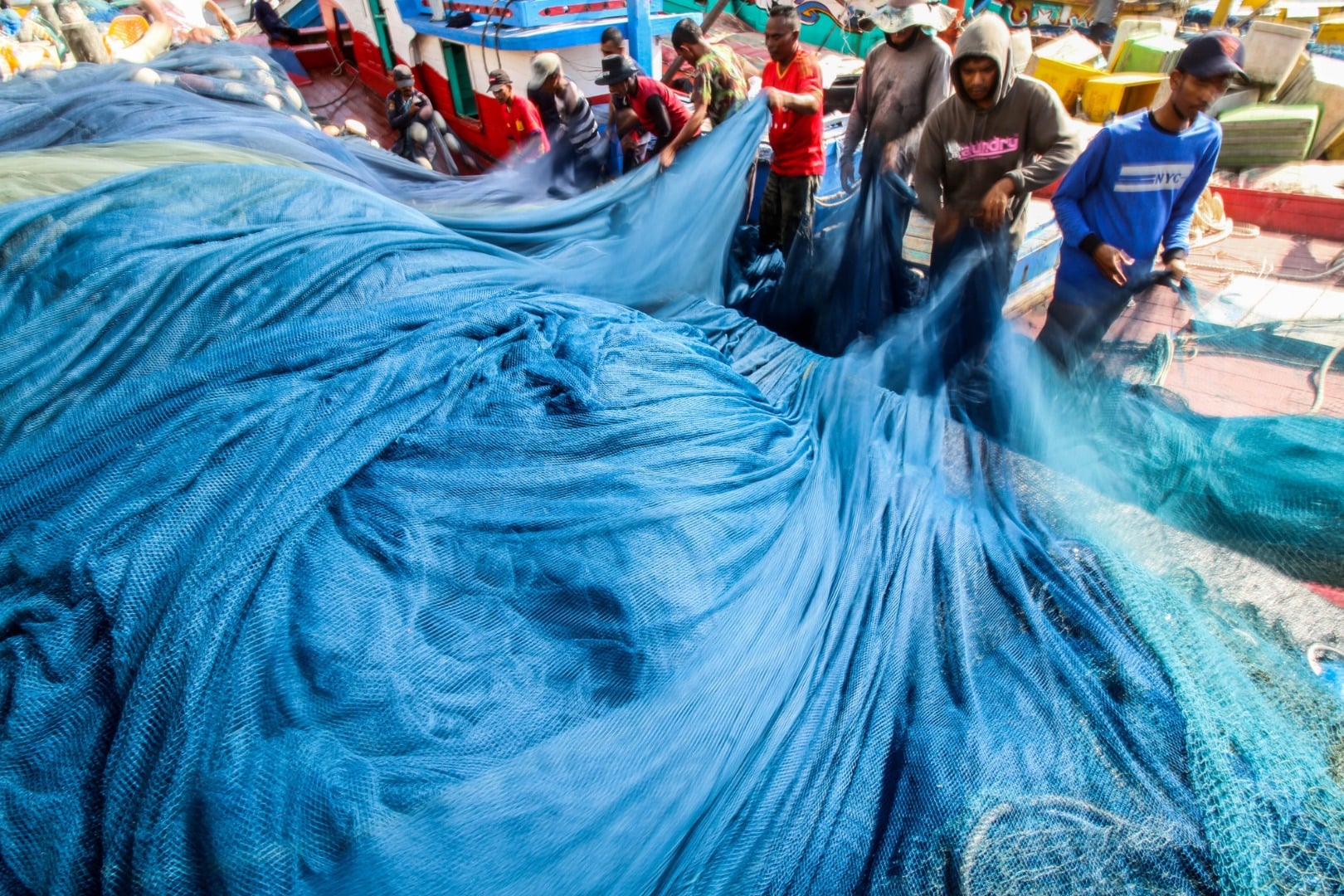 Buruh nelayan merapihkan jaring penangkap ikan