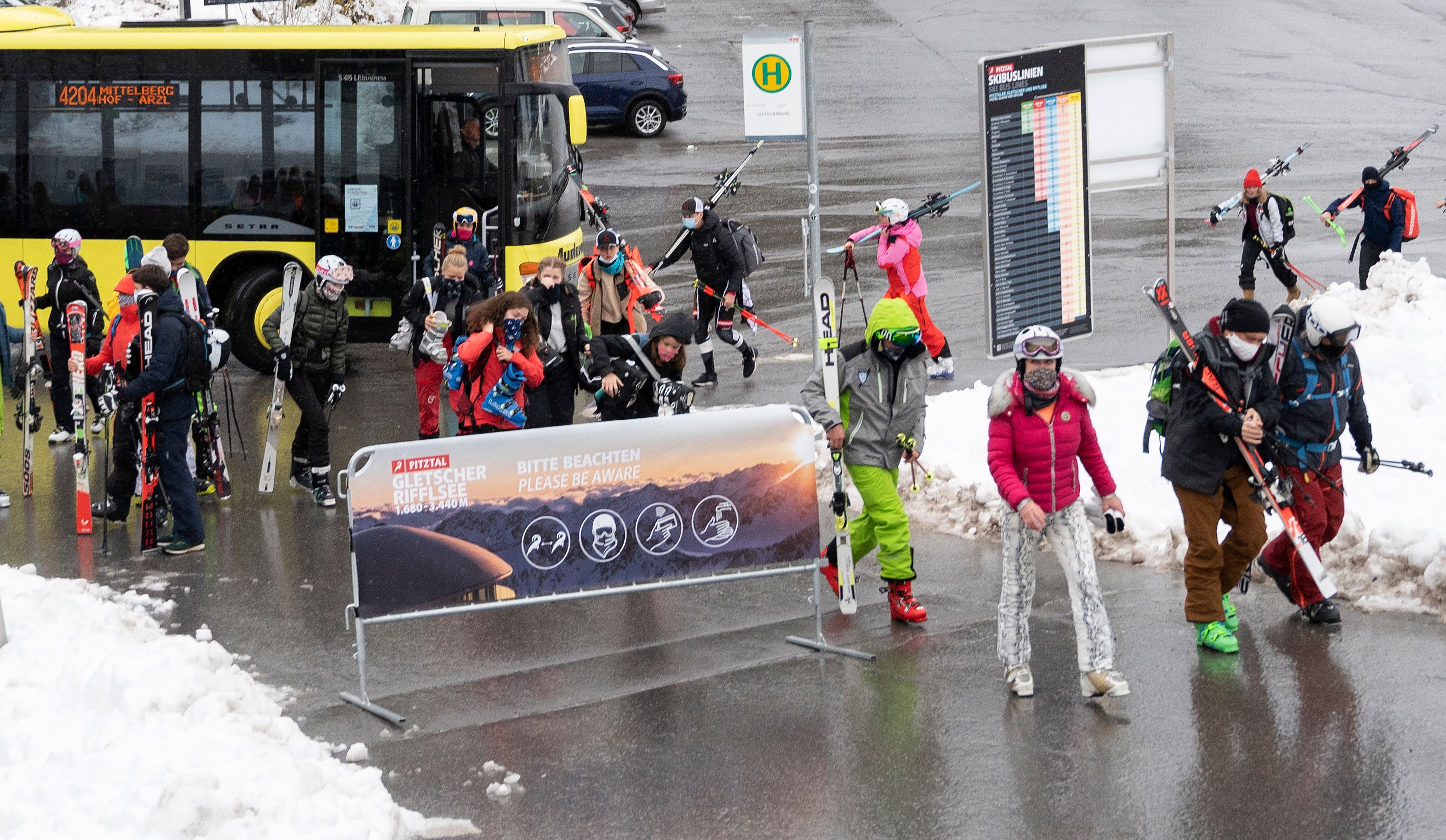 Warga yang akan bermain ski di Austria berjalan melalui papan peringatan mengenai protokol kesehatan covid-19.