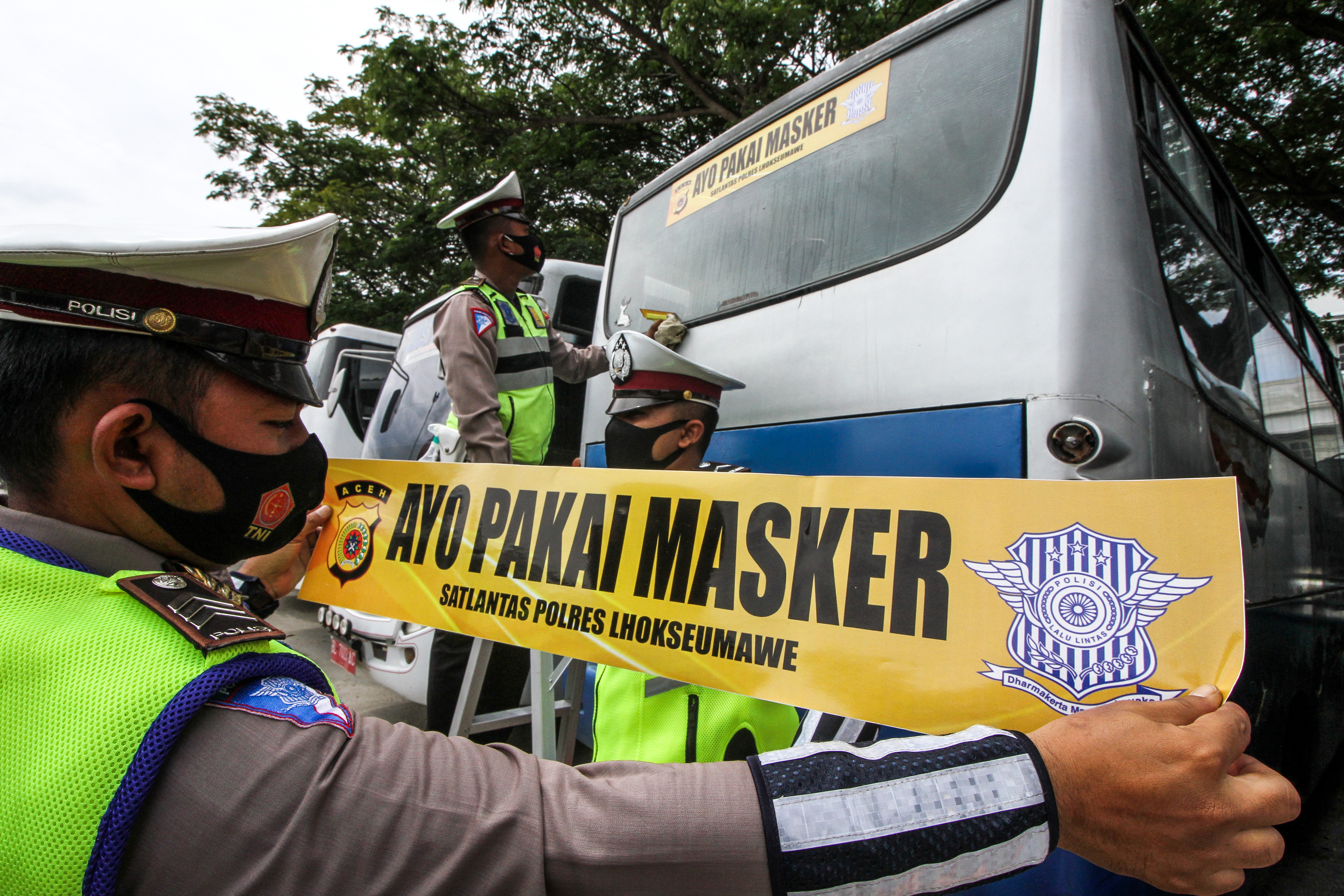 Anggota Polisi Lalu Lintas Polres Lhokseumawe menempelkan stiker Ayo Pakai Masker di sejumlah bus di Terminal Lhokseumawe, Aceh.