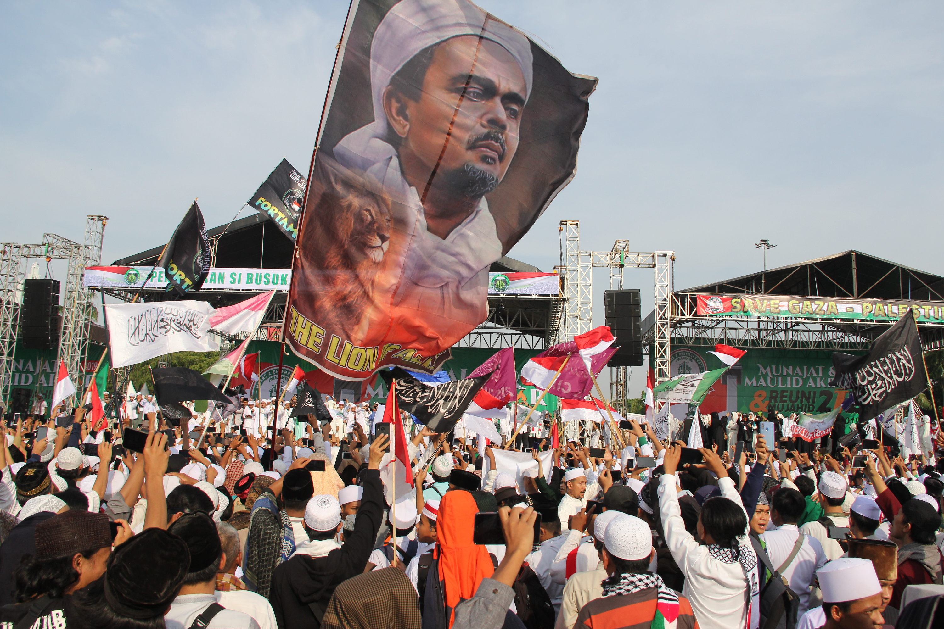Peserta aksi reuni PA 212 membentangkan bendera bergambar wajah Rizieq Syihab di kawasan Monas.