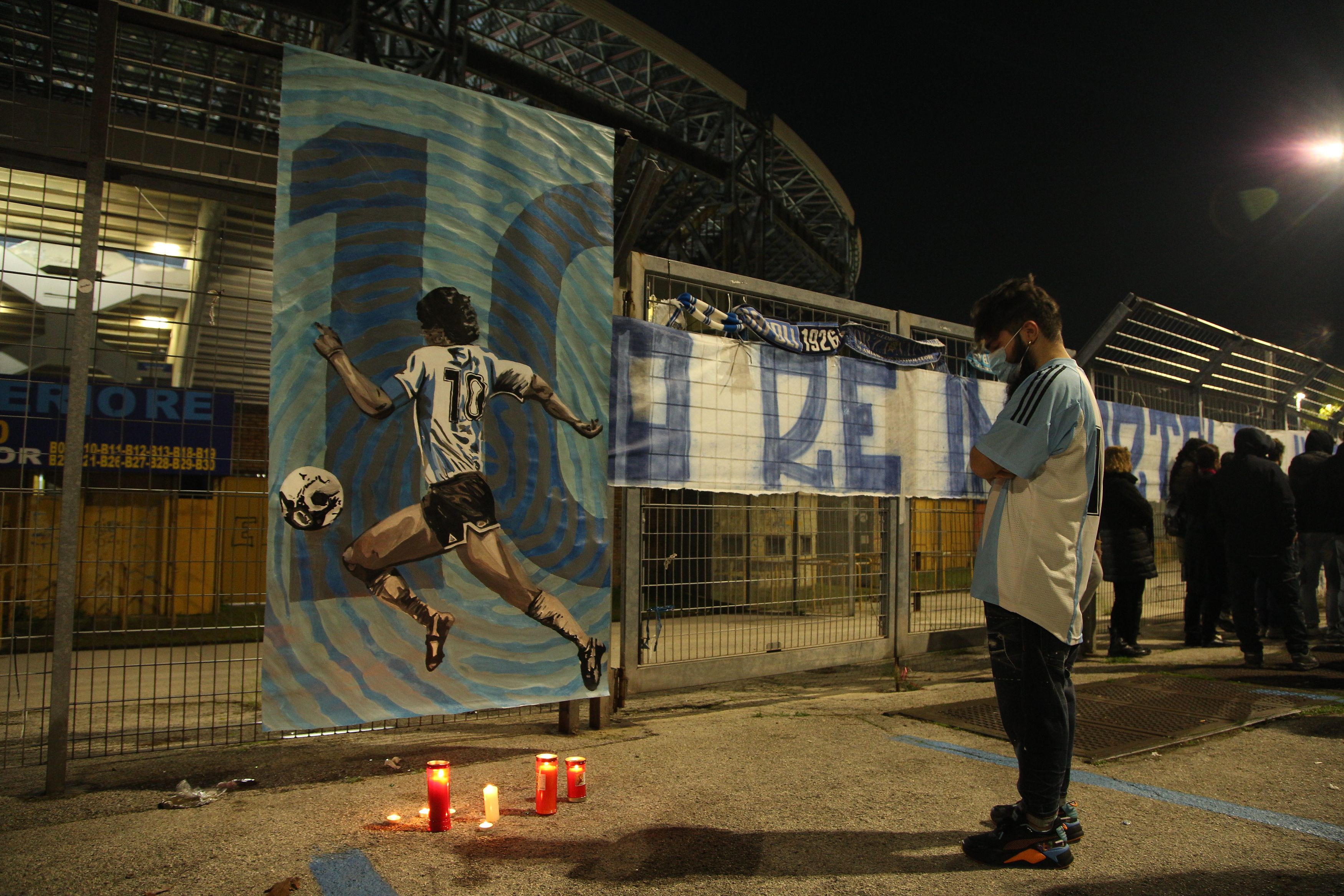 Seorang pemuda berdoa di depan poster Diego Maradona yang dipasang di pagar stadion San Paolo, Napoli, Italia, Rabu (25/11/2020)