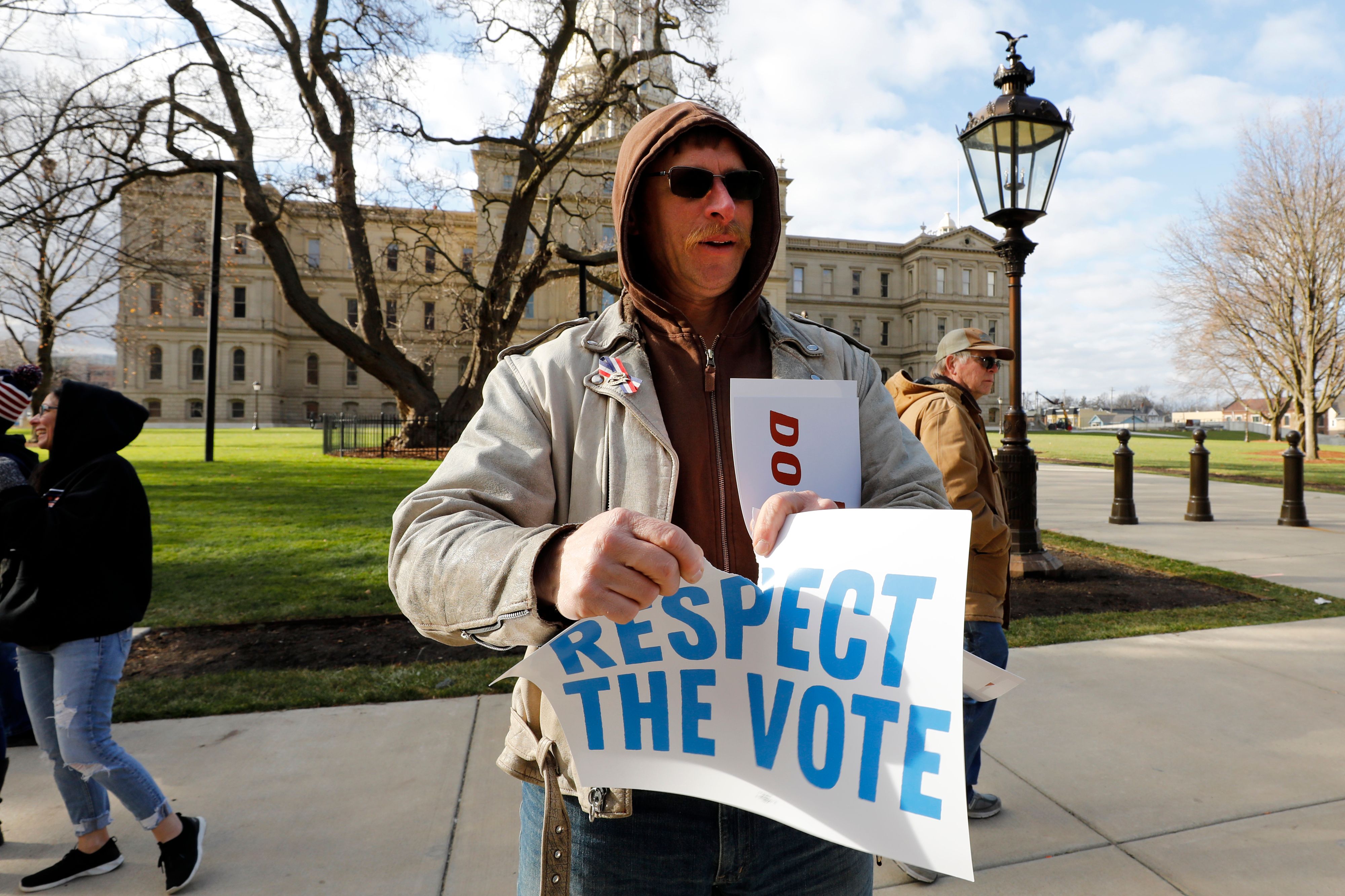 Pendukung Donald Trump merobek spanduk yang dibawanya setelah Pemerintah Michigan menetapkan Joe Biden sebagai pemenang.
