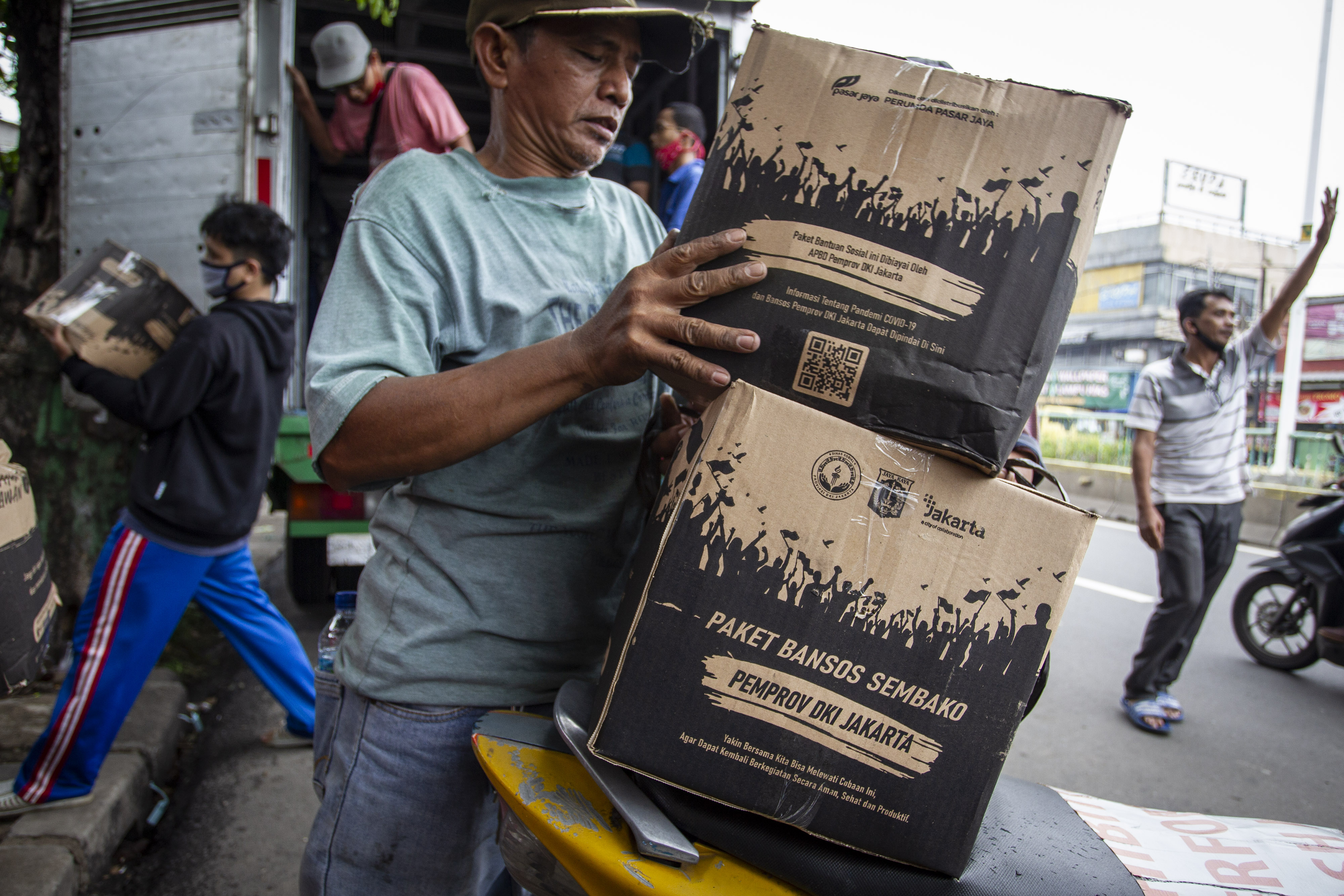 Warga membawa Bantuan Sosial (Bansos) dari Pemprov DKI Jakarta untuk penanganan COVID-19 di kawasan Jatinegara
