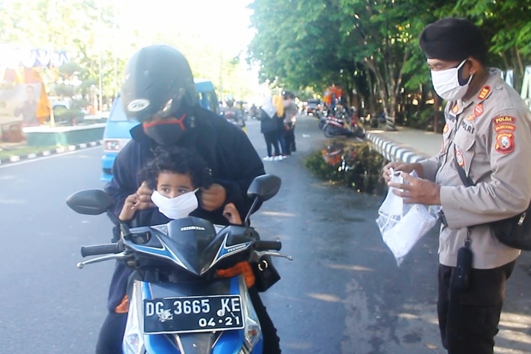 Pengendara roda dua yang tidak menggunakan masker diberikan masker oleh anggota polisi.