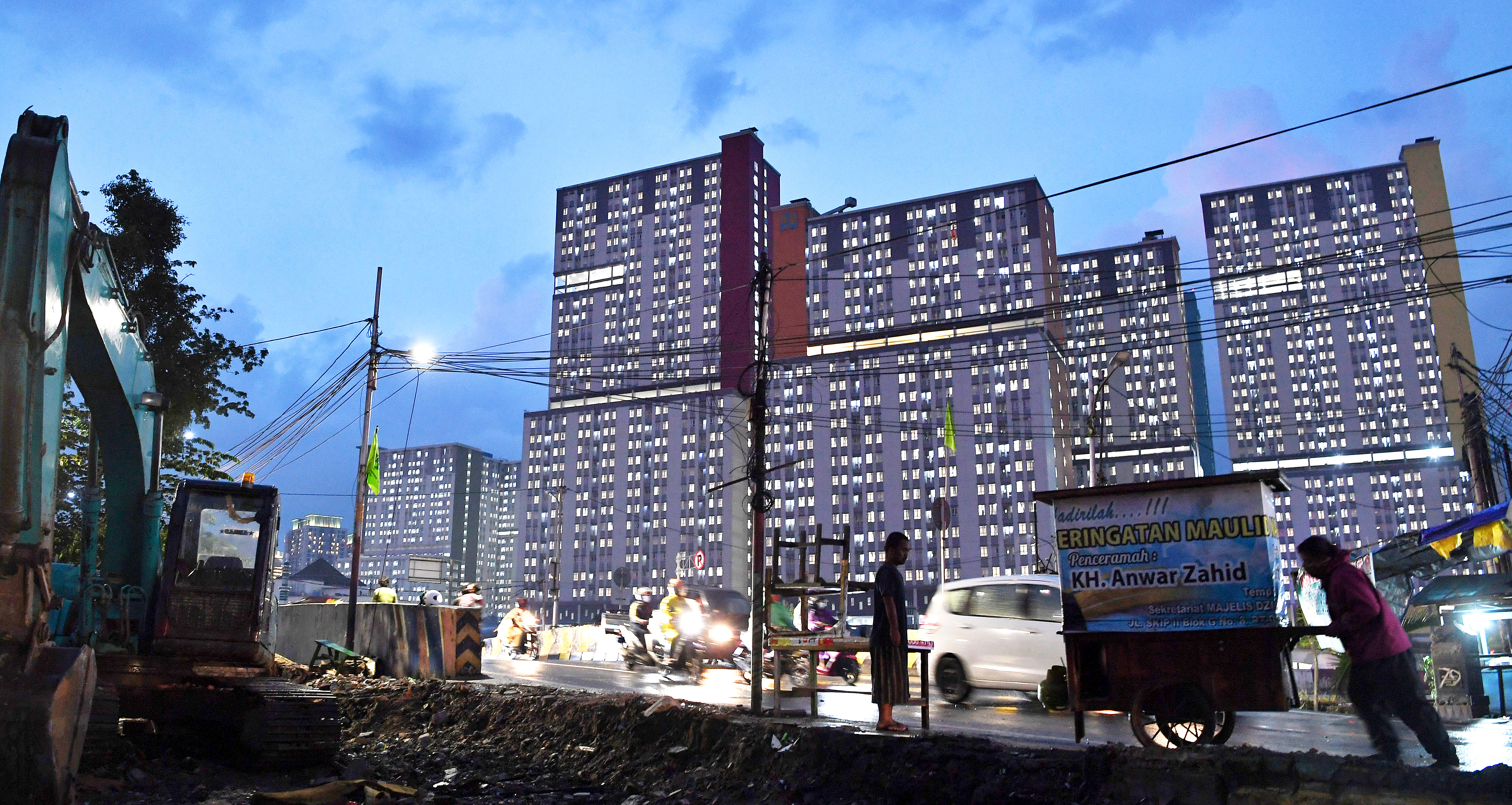 Warga beraktivitas dengan latar belakang Rumah Sakit Darurat Covidi-19 Rumah Sakit Darurat COVID-19 Wisma Atlet di Jakarta