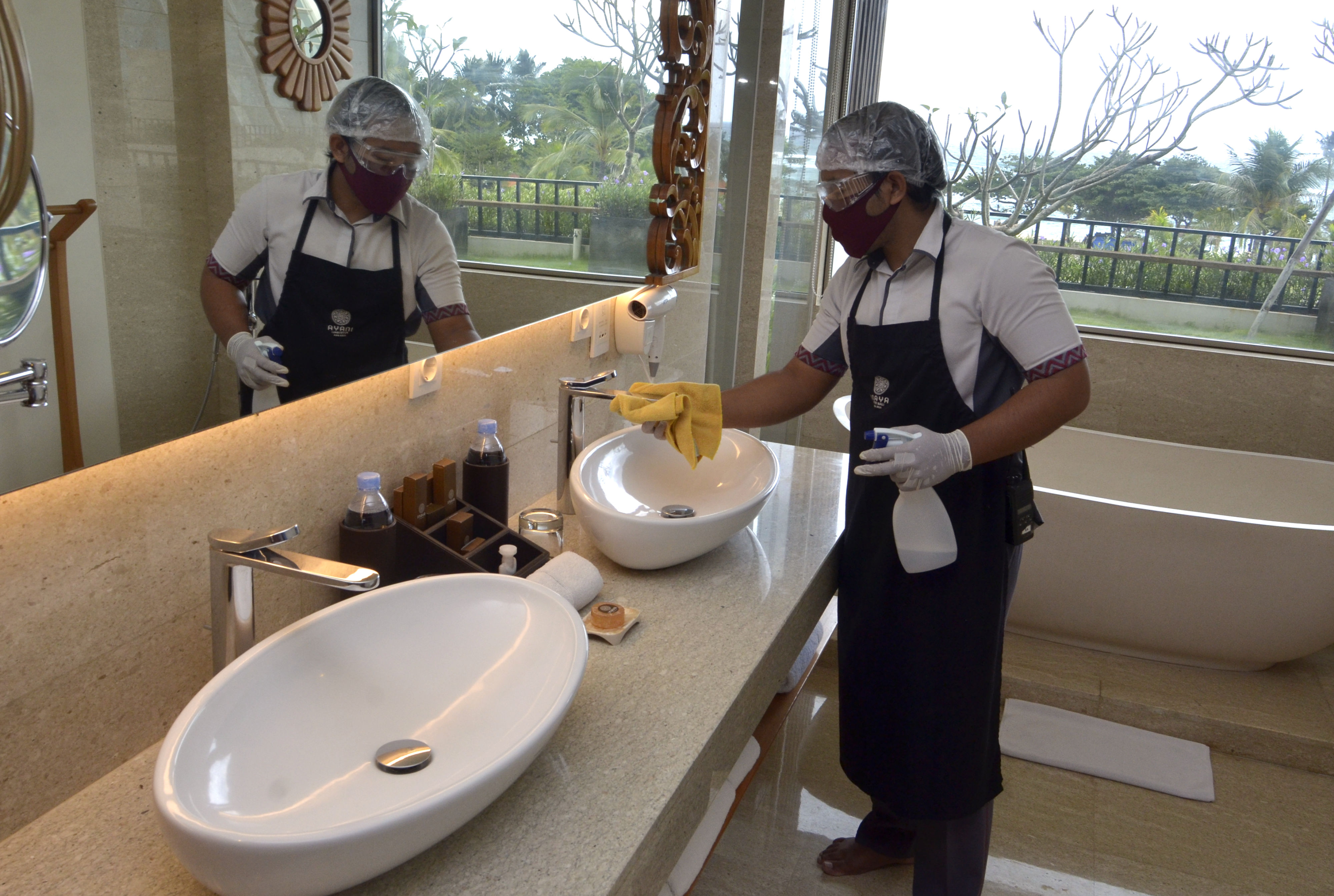 Pekerja menggunakan alat pelindung diri saat membersihkan kamar di Hotel Inaya Bali.