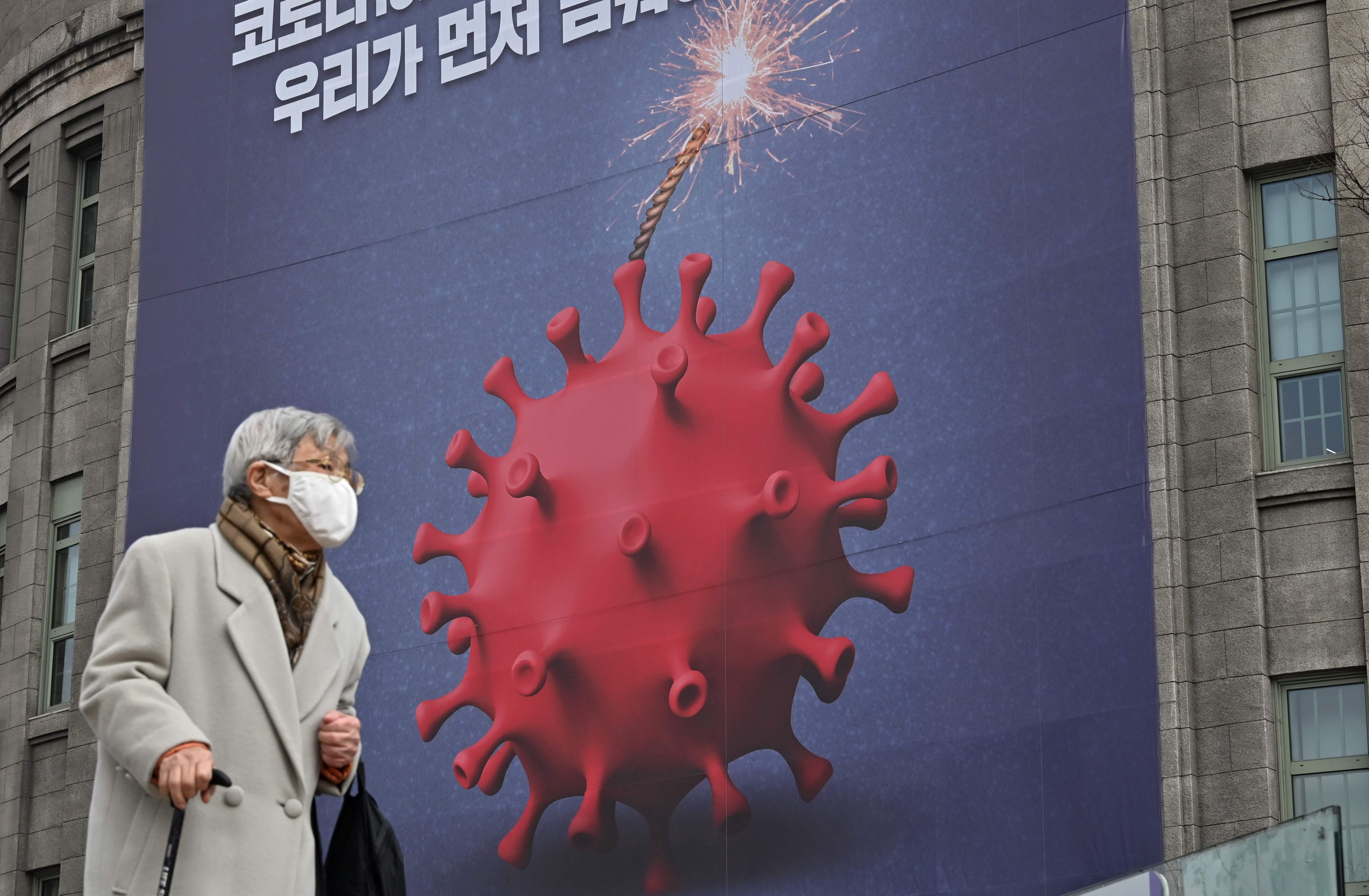 Seorang wanita tua berjalan melewati poster yang menggambarkan virus corona sebagai bom untuk memperingatkan terhadap virus corona Covid-19 