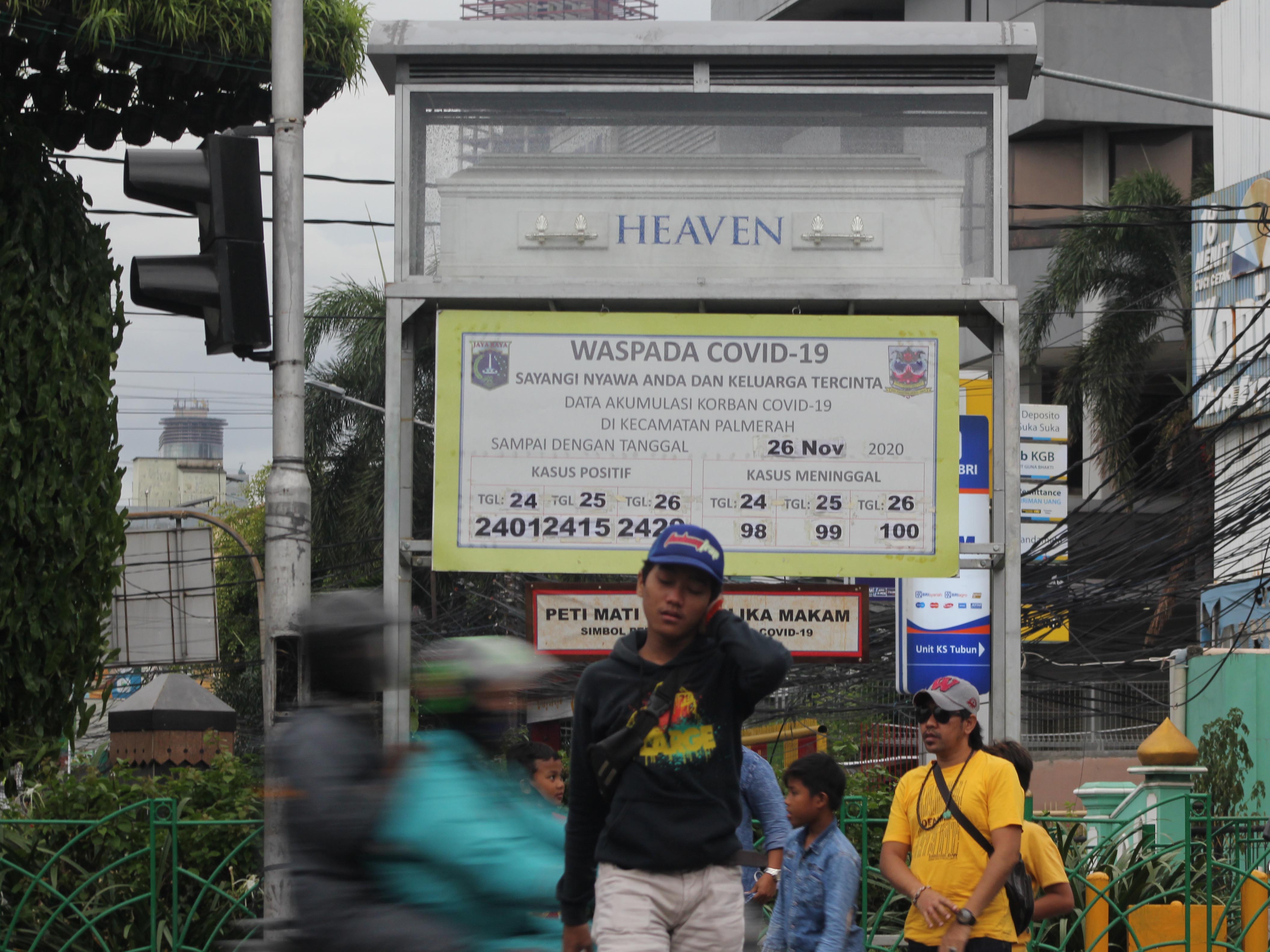 Pengguna jalan melintasi tugu Simbol Peringatan Bahaya covid-19 di Jalan KS Tubun, Jakarta.
