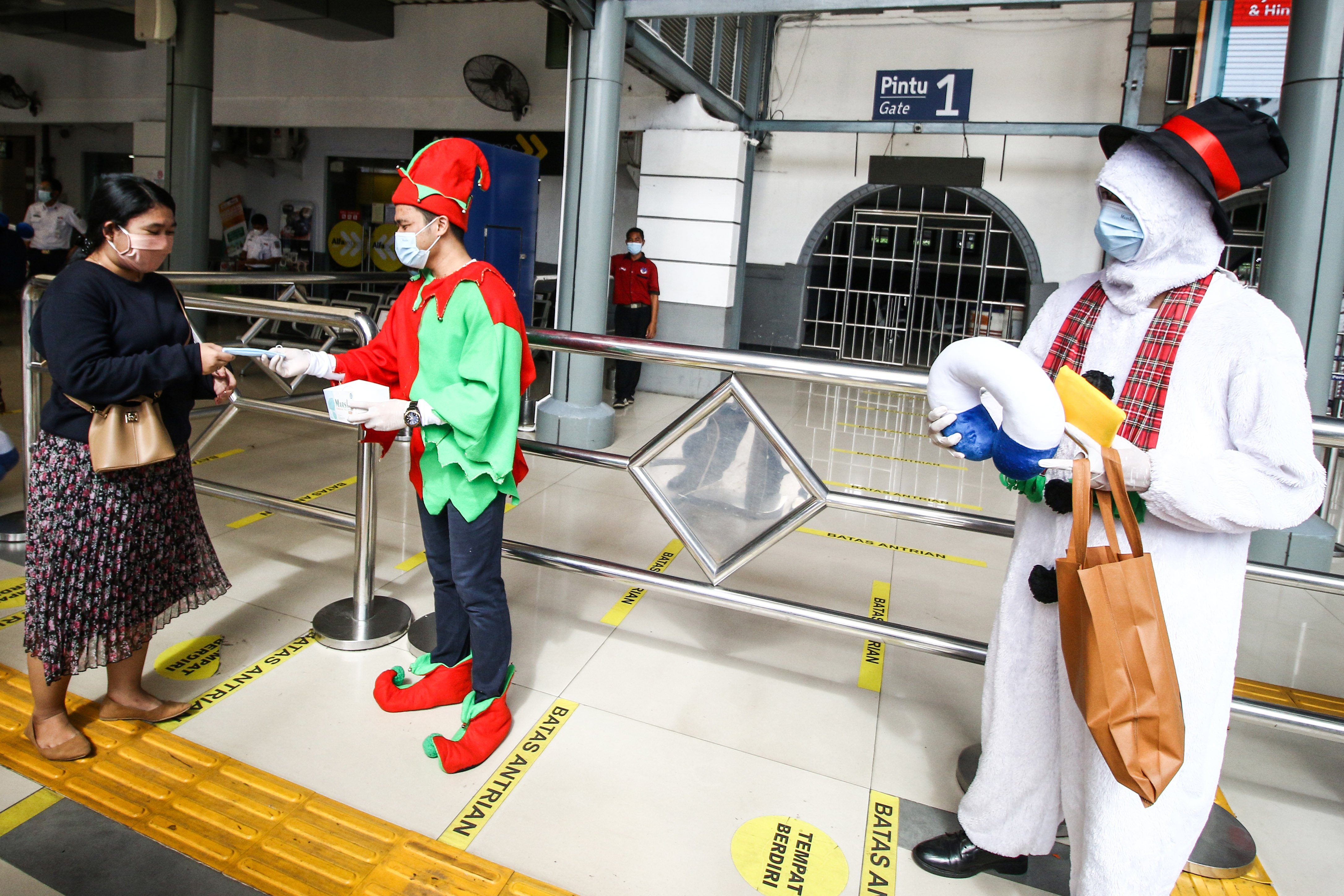 Petugas memakai kostum bertema Natal membagikan masker ke penumpang di Stasiun Pasar Senen, Jakarta, Jumat (25/12)