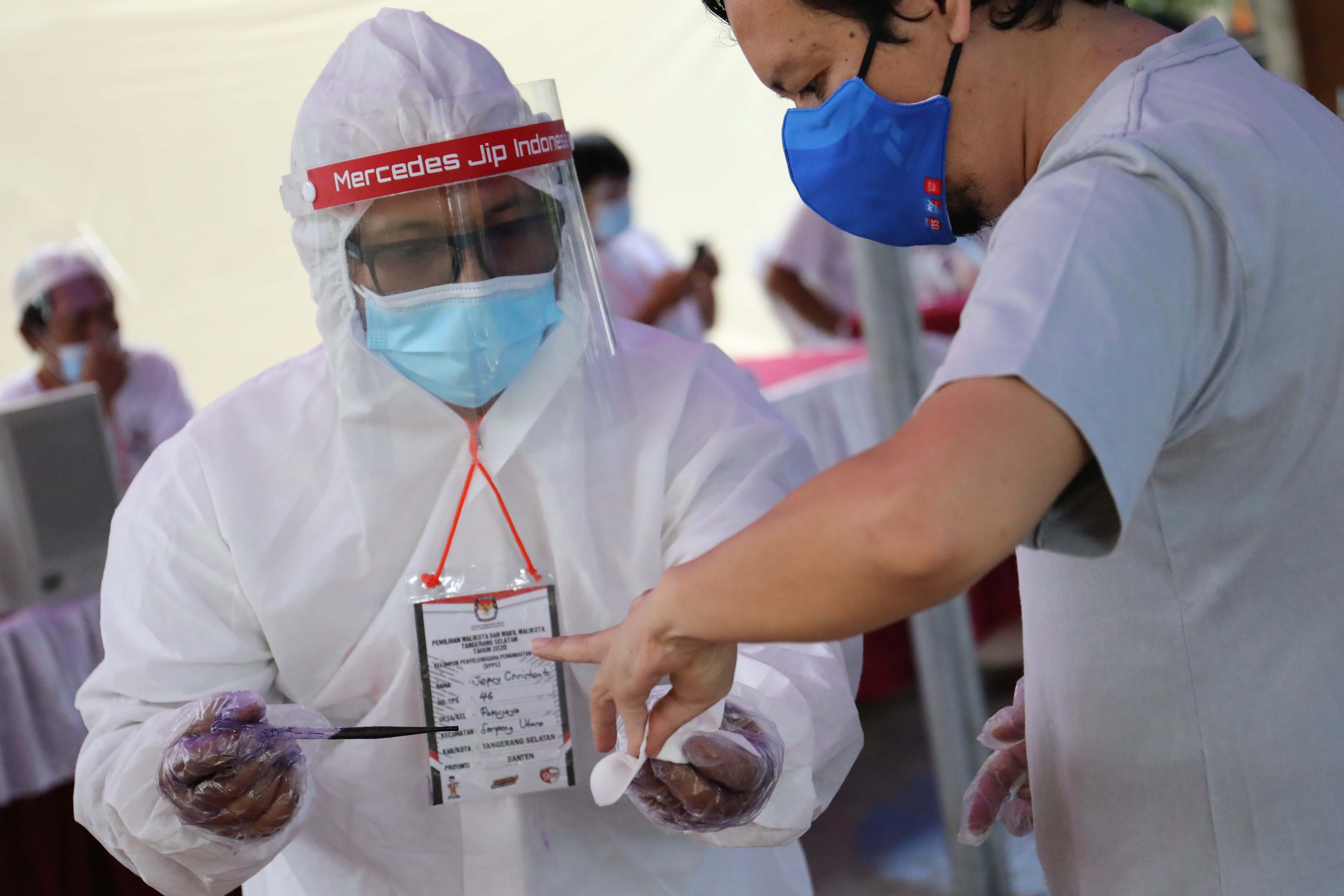 Ilustrasi: Petugas kelompok penyelenggara pemungutan suara (KPPS) menggunakan APD mendampingi pemilih memasukkan kertas suara