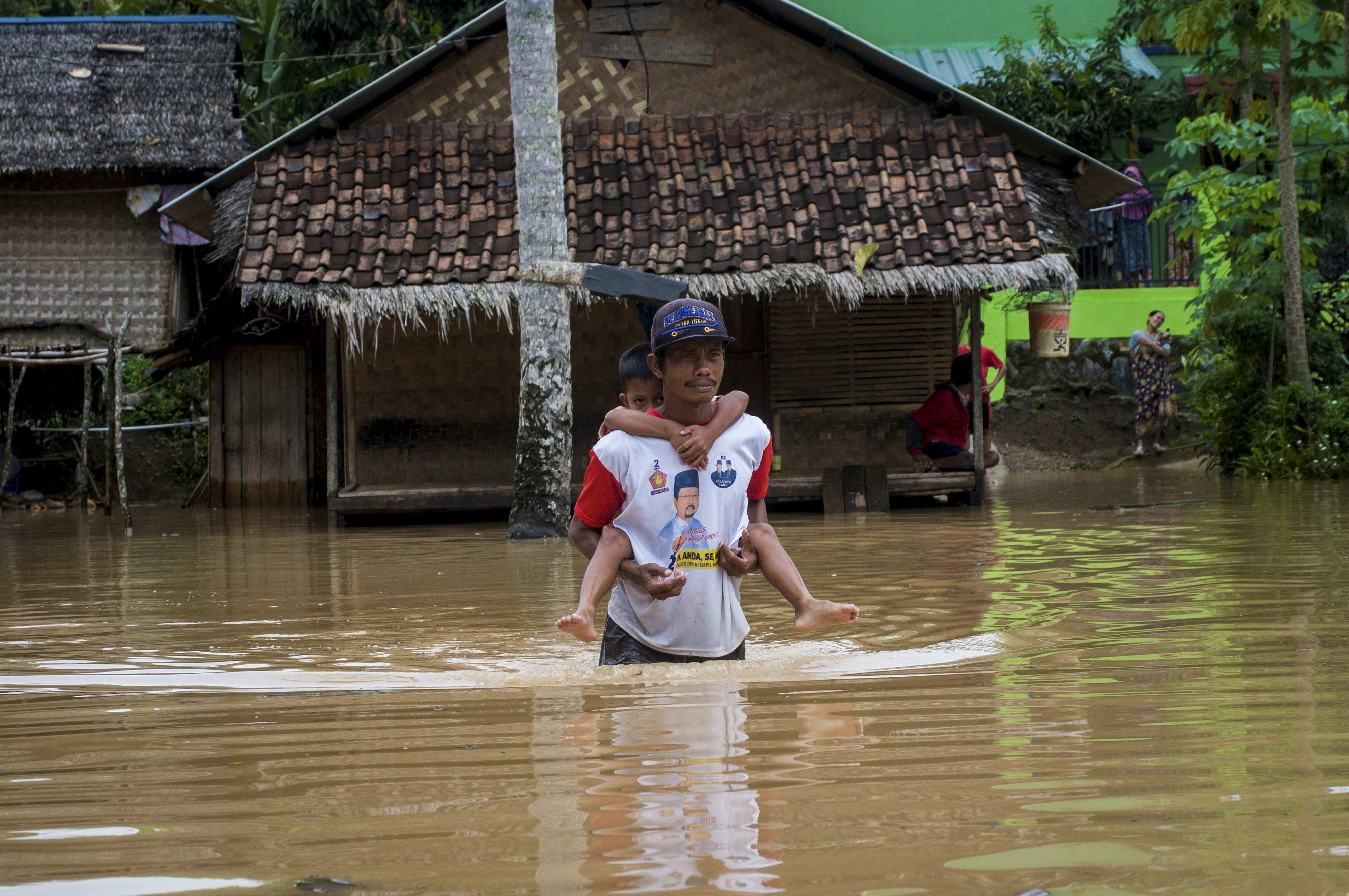 Seorang bapak menggendong anaknya saat menembus banjir di Desa Keusik, Lebak, Banten, Kamis (3/12).
