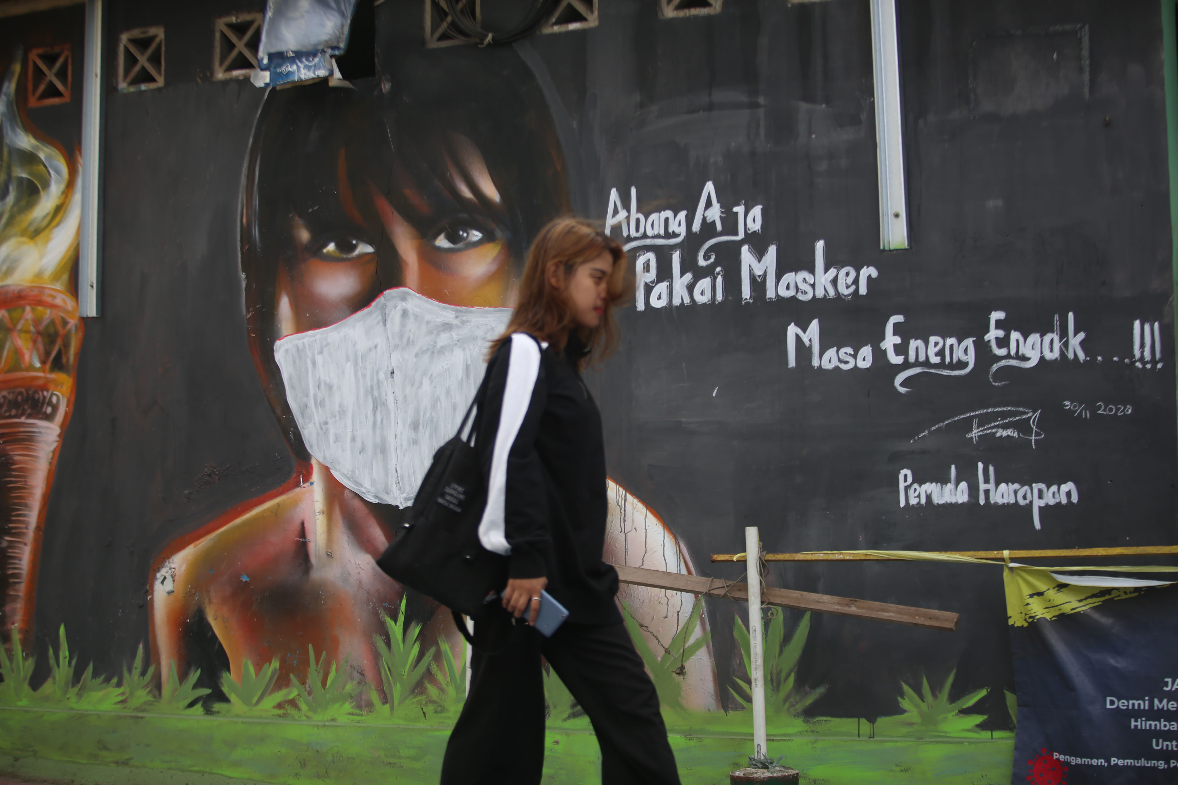 Warga melintas di depan mural berisi imbauan disiplin protokol kesehatan di Jakarta.