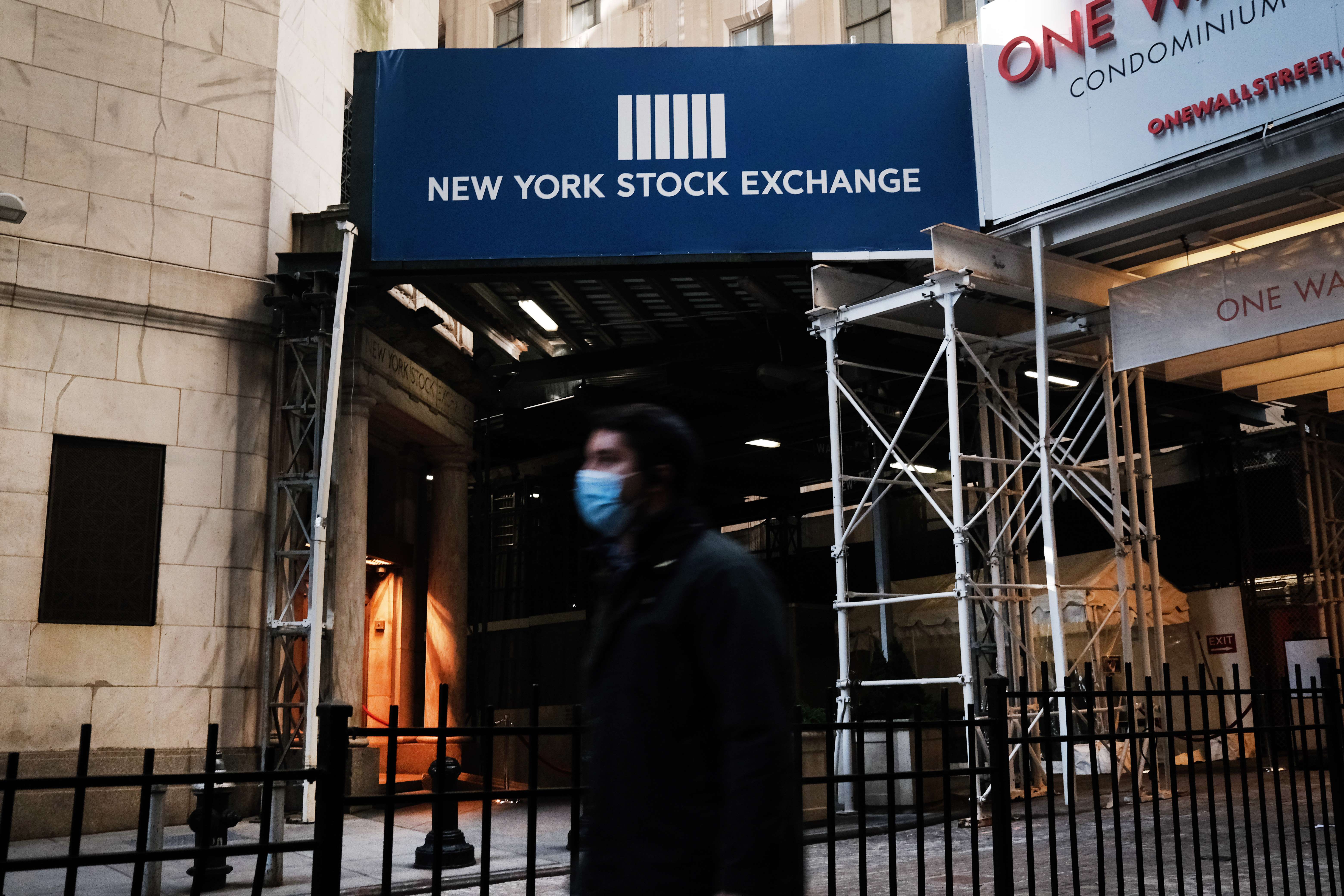 Seorang warga memakai masker berjalan di depan Gedung Bursa Saham New York, AS. Pasar menyambut paket stimulus AS dengan beragam.